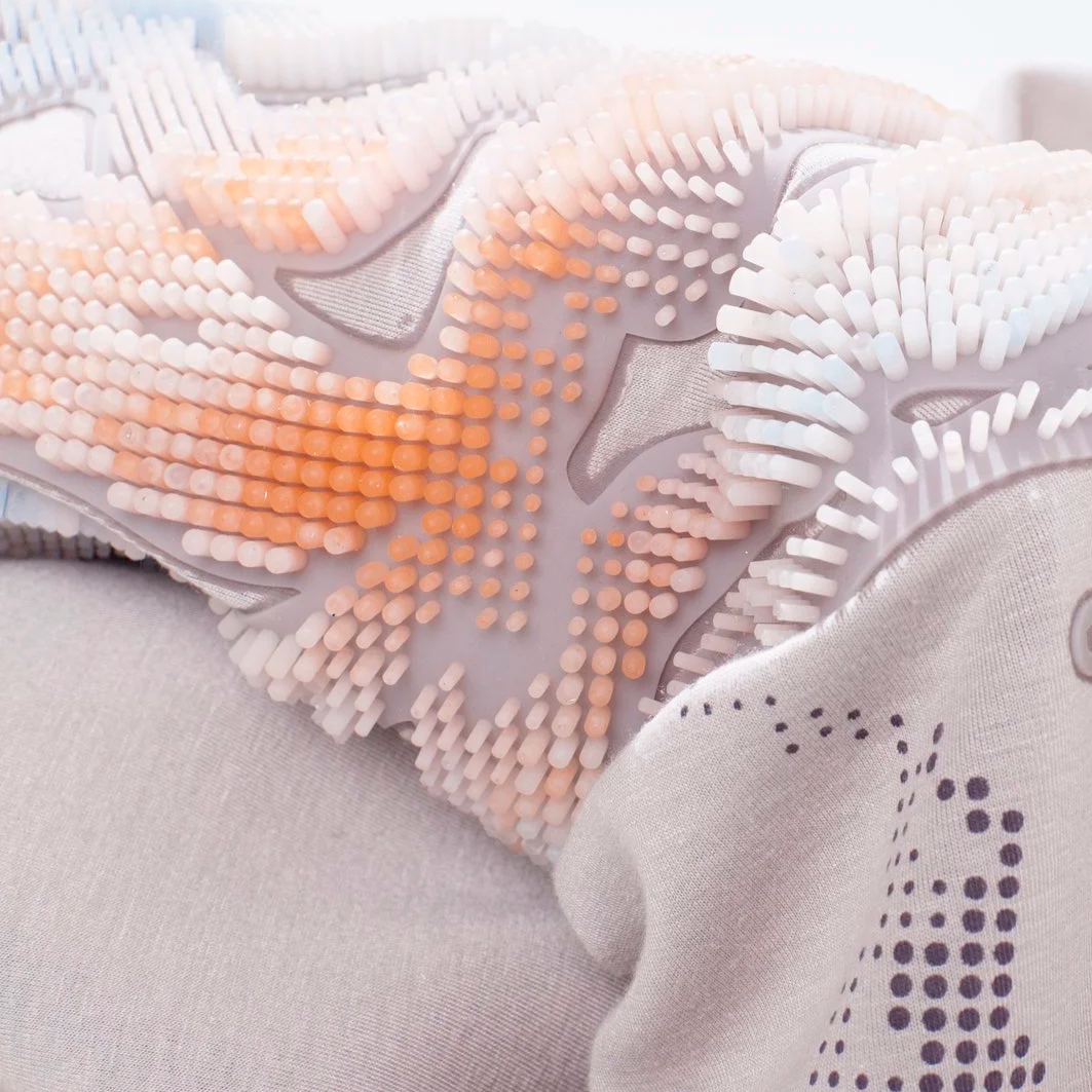 Close-up of a textured hand-cast silicone textile with soft, flexible, ridged bumps in white, pale blue, and light orange colors.