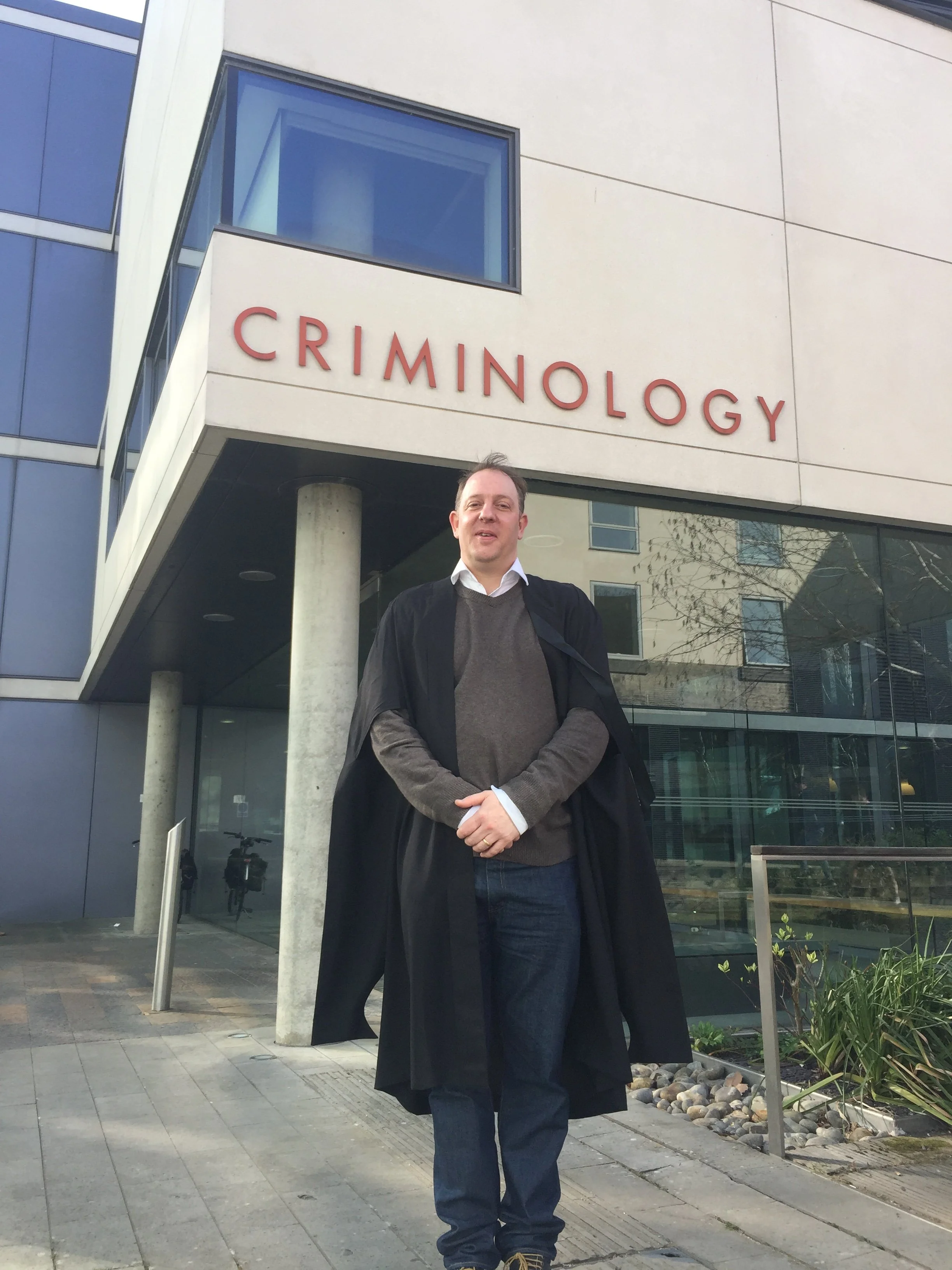 A man standing outside of a modern building with large glass windows and a sign that reads 'CRIMINOLOGY' on the wall behind him.