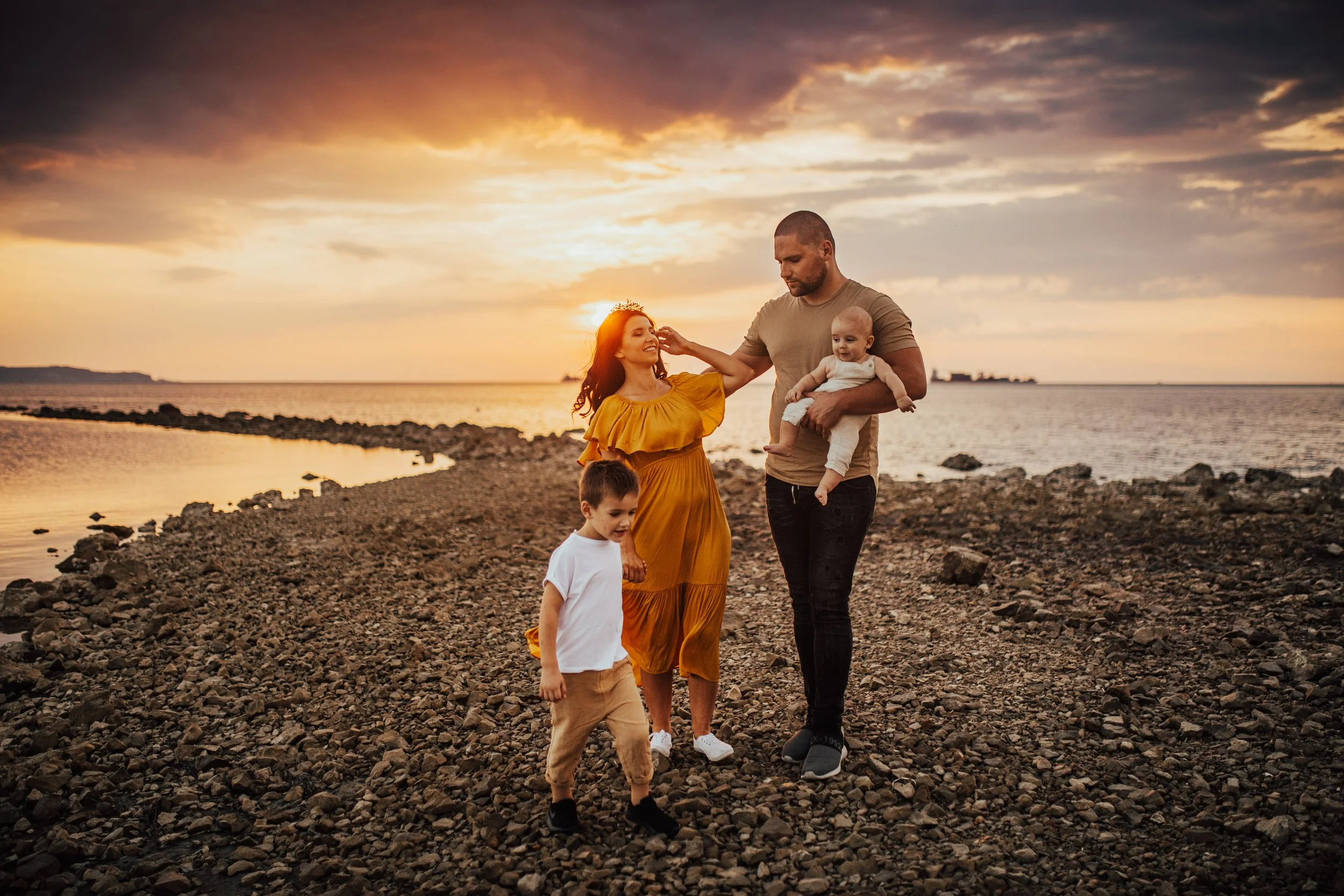 A family of five walking on a rocky beach during sunset, with the sky partly cloudy and the ocean in the background.