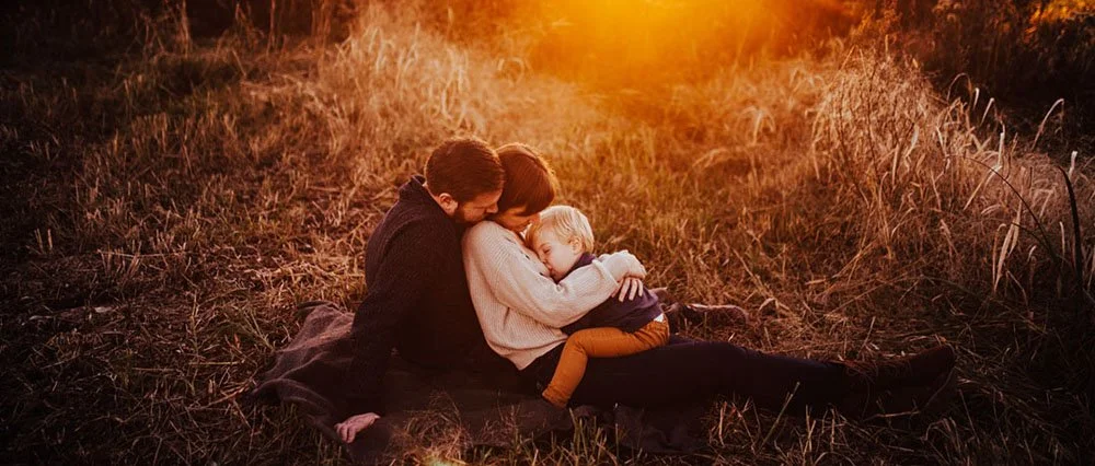 A family sitting on a blanket in a field during sunset, cuddling and embracing each other warmly.
