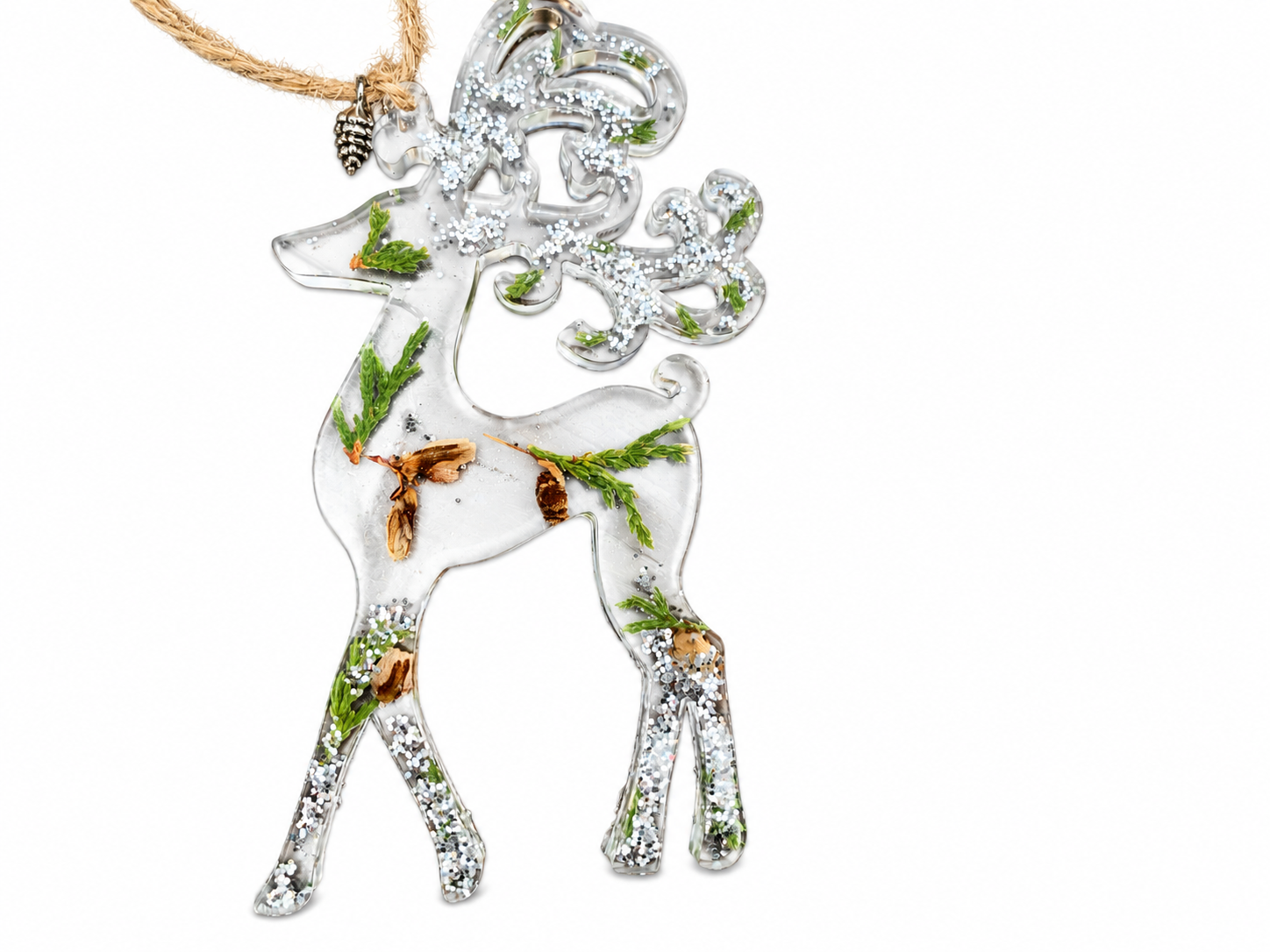 Handmade clear resin reindeer Christmas ornament with decorative antlers, real preserved greenery, natural pine cone pieces and shimmering silver accents on a white background.