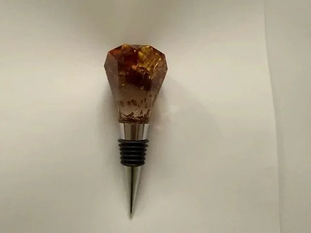 Handmade botanical wine stopper with preserved strawflower petals in warm amber toned resin, shaped into a geometric crystal design.