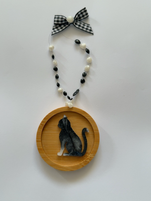 Handmade black and white resin cat Christmas decoration sitting in profile on a 6.5 cm round wooden ornament, finished with decorative black and white beads and a gingham ribbon bow.