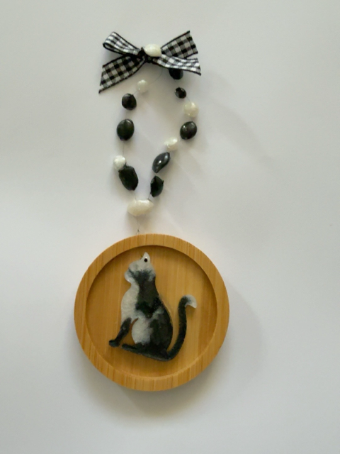 Handmade black and white resin siiting cat Christmas decoration on a 6.5 cm round wooden ornament, finished with black and white beads and gingham ribbon bow.
