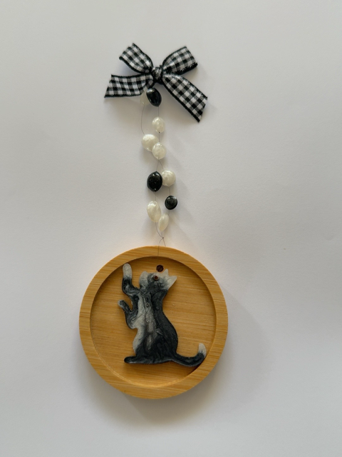 Handmade black and white resin cat Christmas decoration reaching upwards with both paws raised, on a 6.5 cm round wooden ornament with black and white beads and a gingham bow.