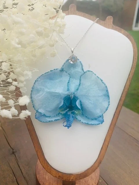 Handmade real blue orchid flower necklace coated in clear UV resin, displayed on a jewellery stand.