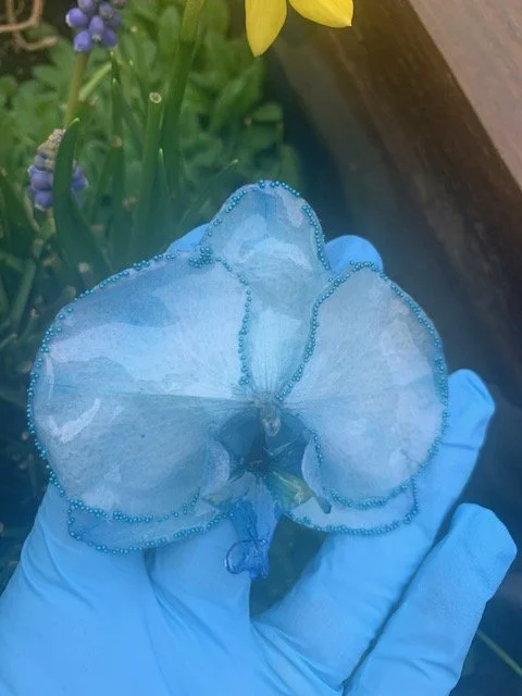 Detailed close up of a real blue orchid flower preserved with a clear UV resin coating, showing the delicate petals of this handmade botanical necklace.