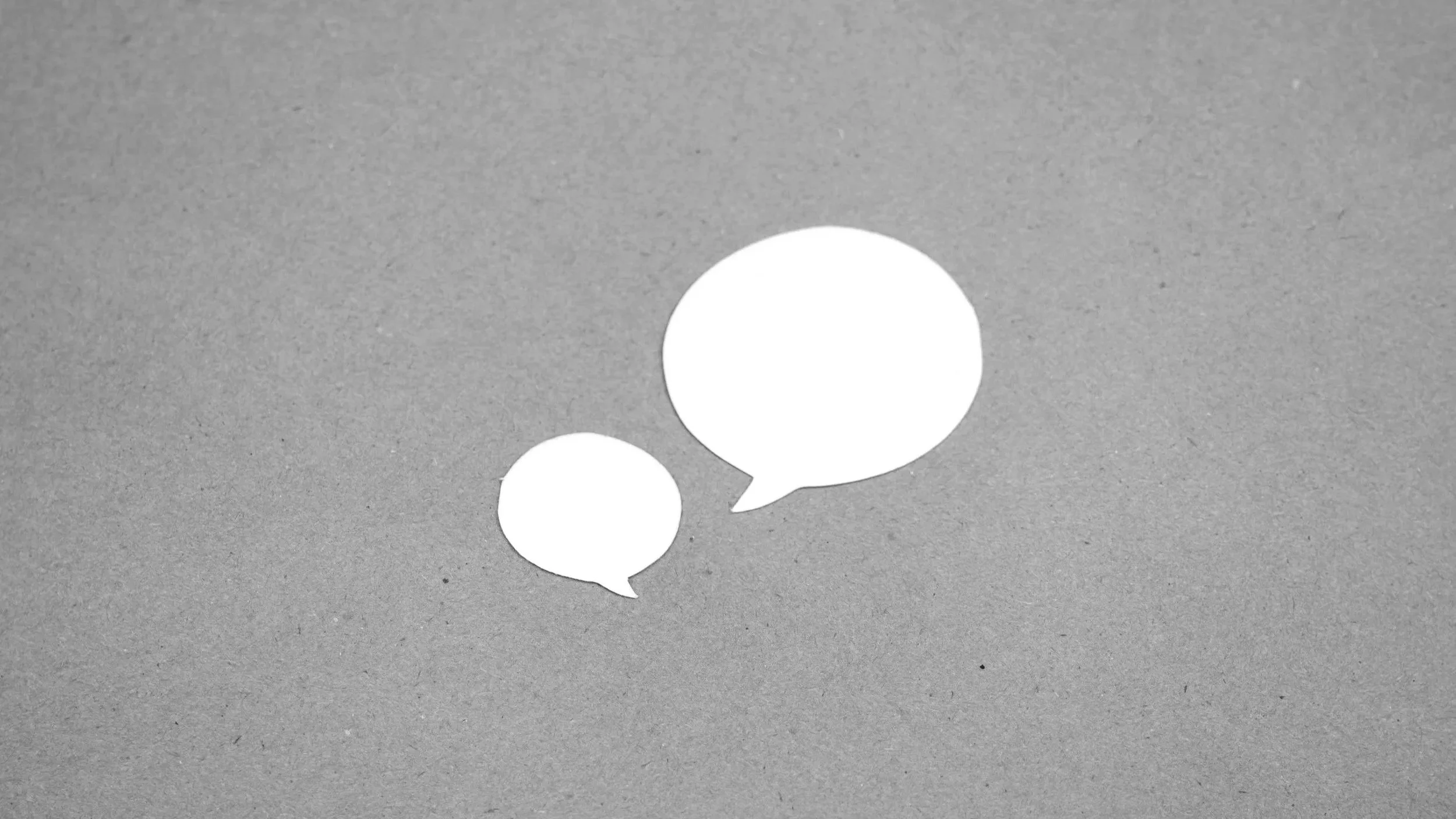 Two speech bubbles placed on a plain, textured gray background.