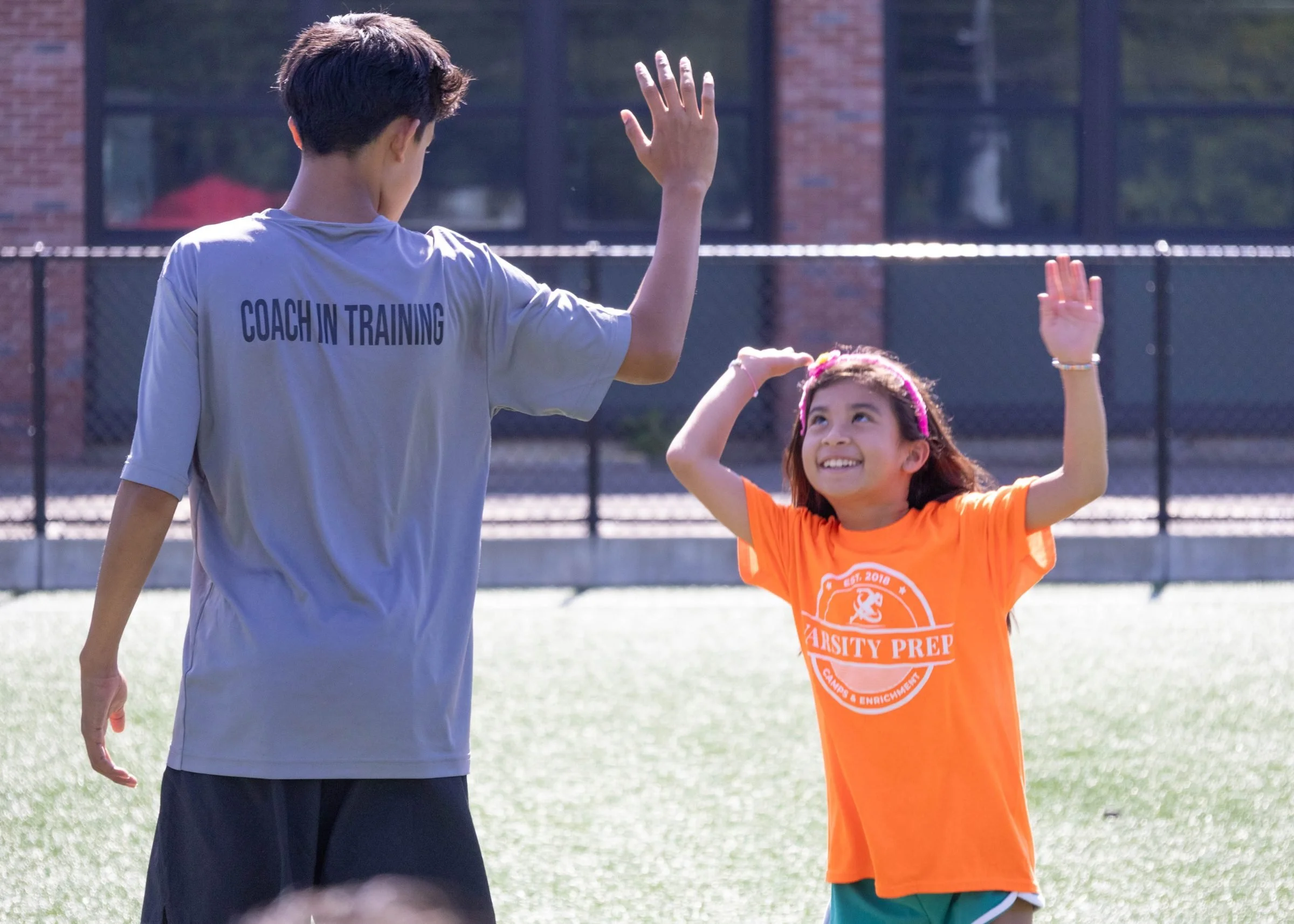 A Coach in Training high-fiving a young camper