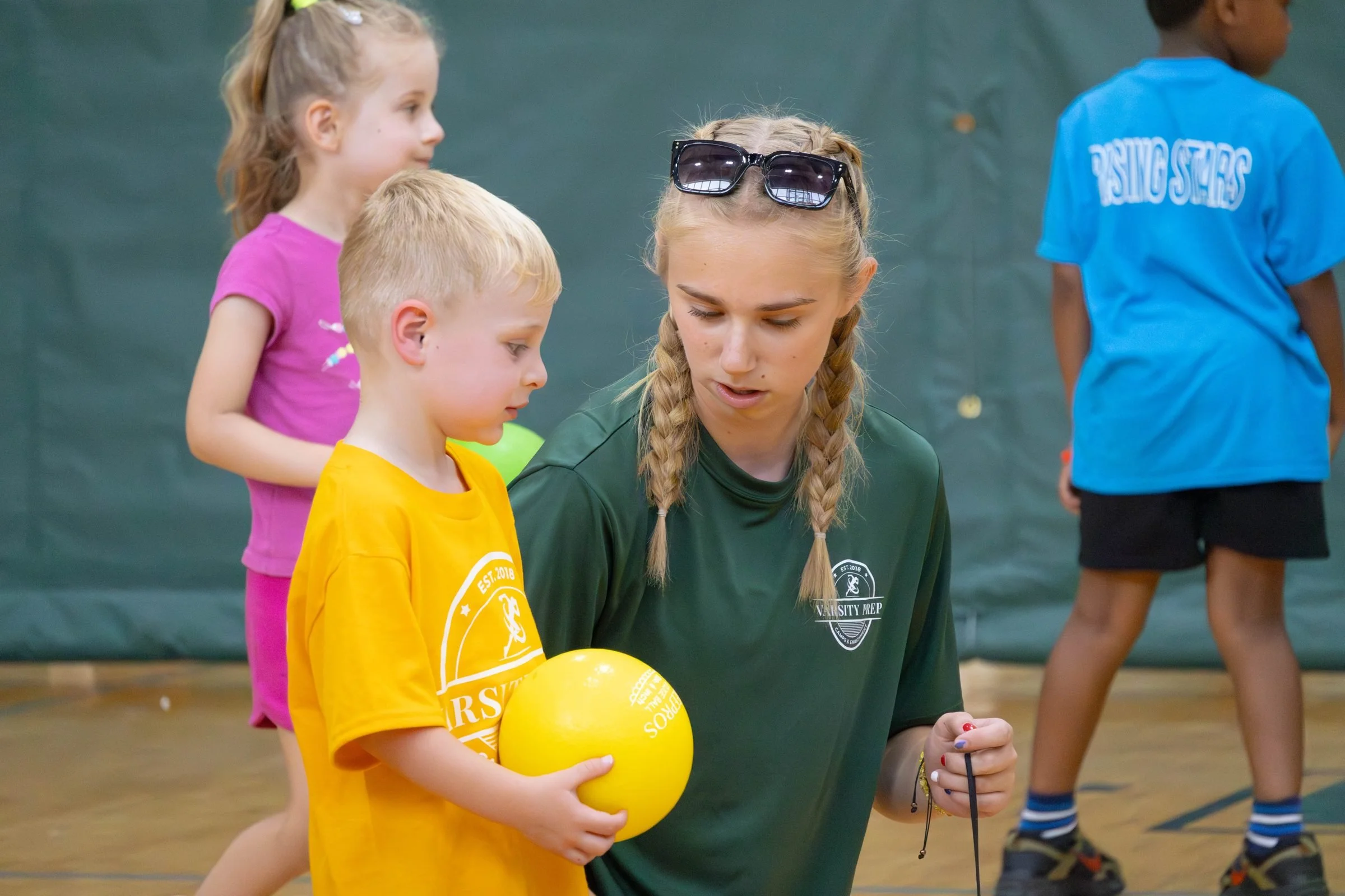 Young camper holding a ball with a counselor in the gym