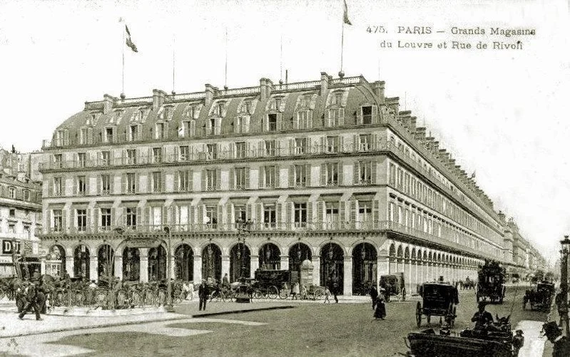ancienne photographie d'un grand bâtiment à Paris, avec des voitures et des gens dans la rue, intitulée 'Grand Magasin du Louvre et Rue de Rivoli'.