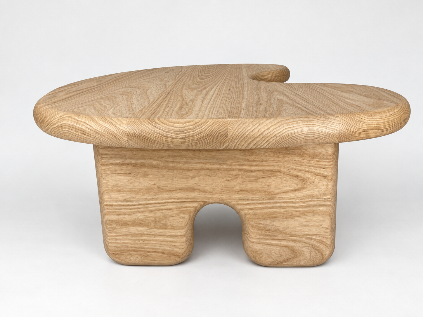 Wooden table with an abstract, organic shape, light wood grain, smooth surface, rounded edges, and a unique leg design with two arches.