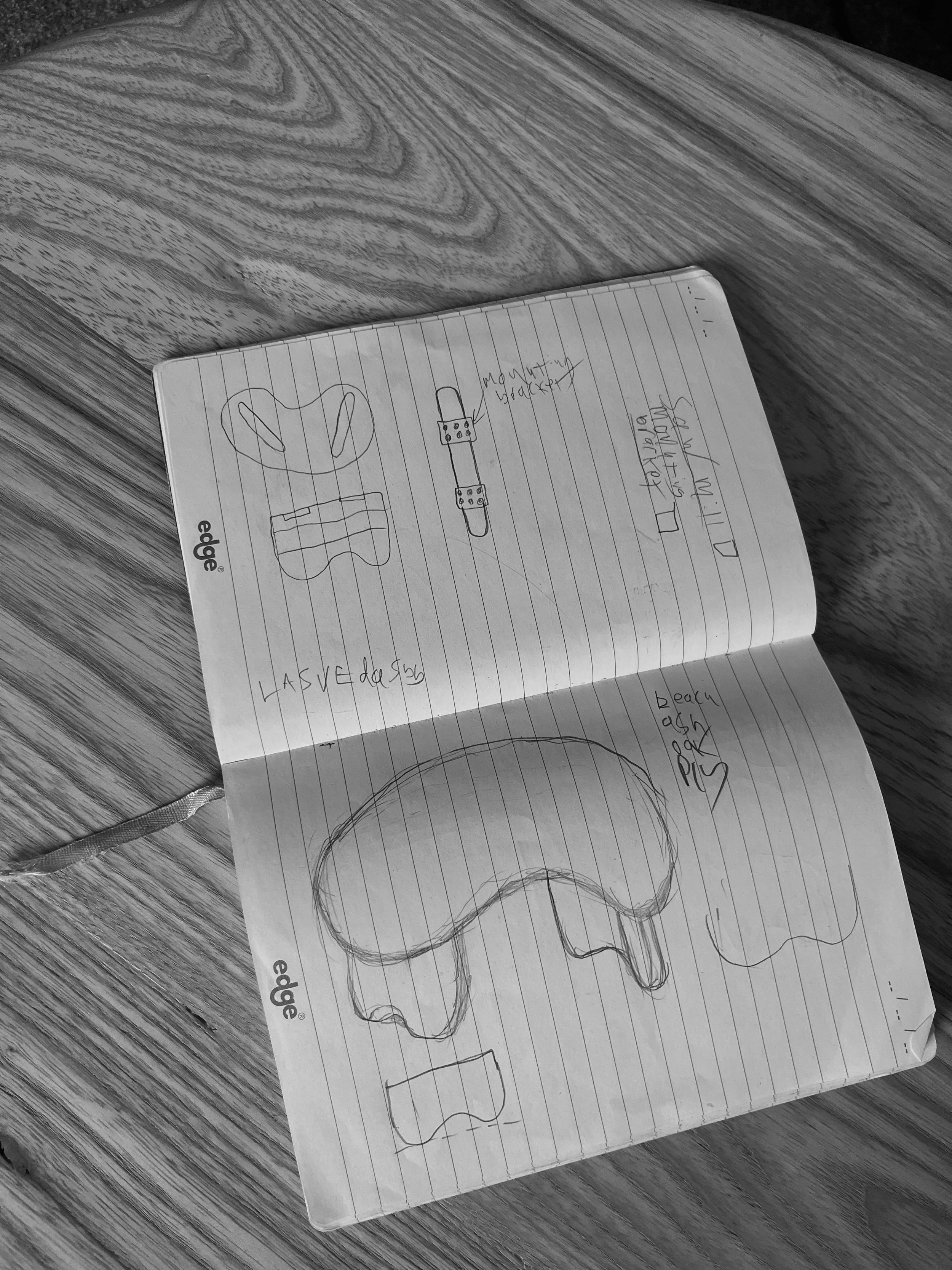 A notebook with sketches of a face, an eyeball, a band-aid, and some handwritten notes on a wooden surface.