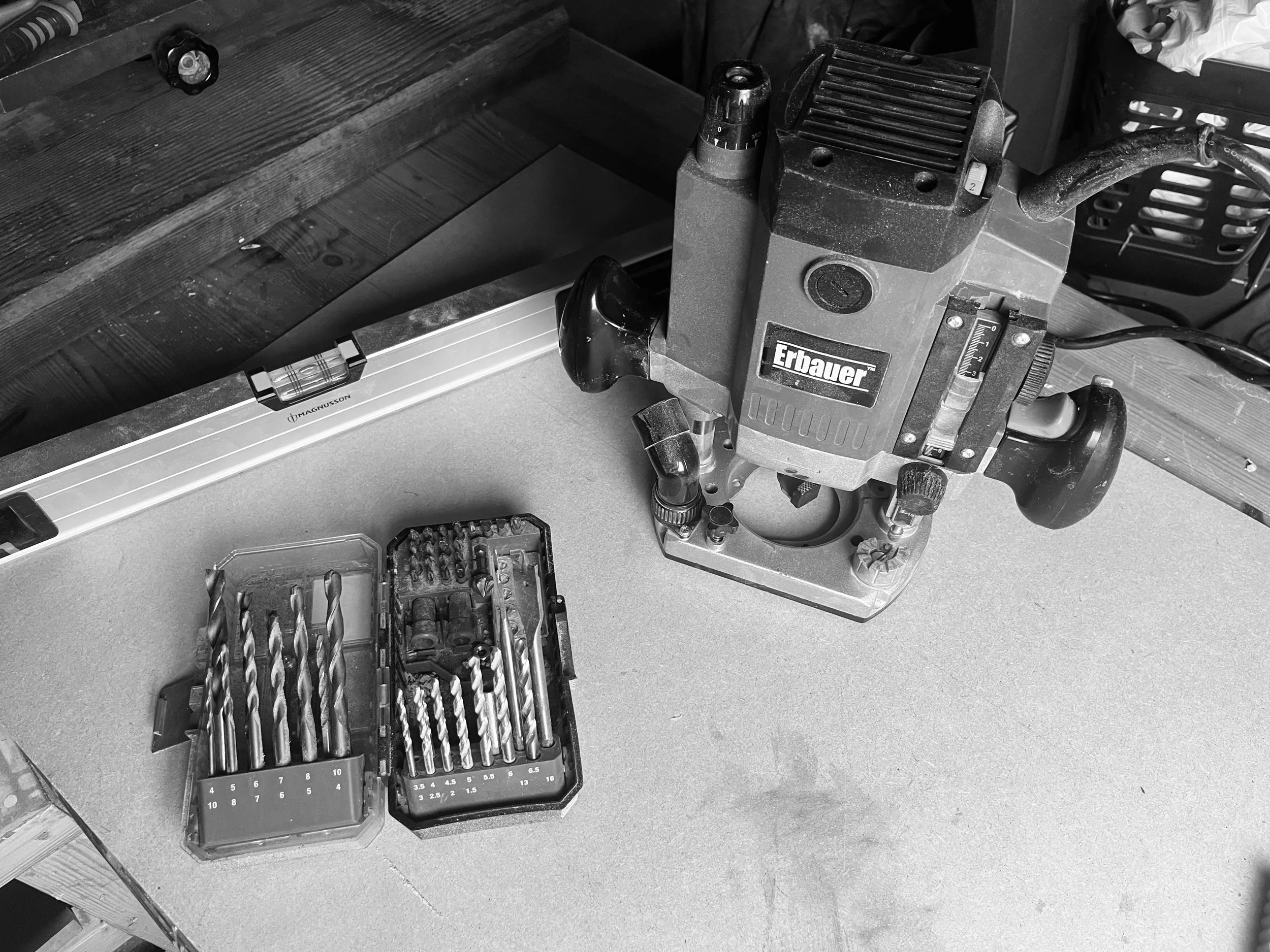 A workbench with a power drill, drill bits in a case, and a level tool.