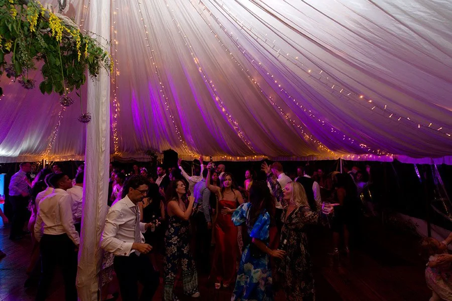 People dancing and socializing under a decorated tent with string lights at a celebration or party.