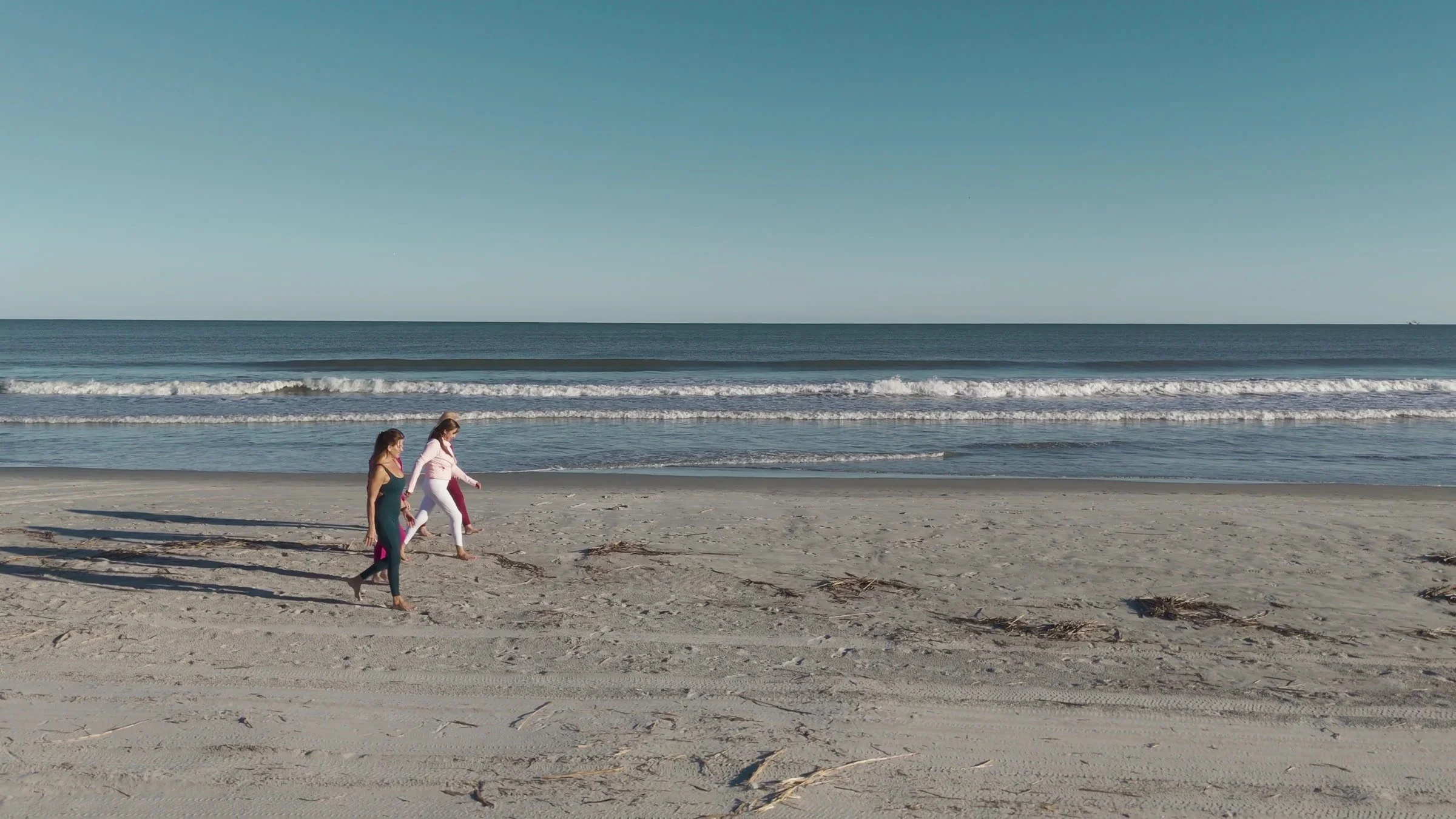 A wide coastal frame with women walking beside the ocean