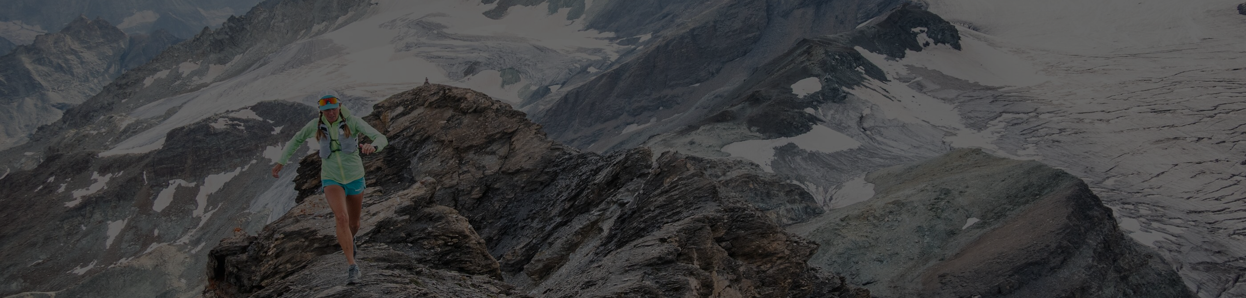 A woman in Patagonia running gear and Oboz hiking footwear or boots balancing on a rocky mountain ridge with snow-capped peaks in the background near Yellowstone National Park and Bozeman, Montana.