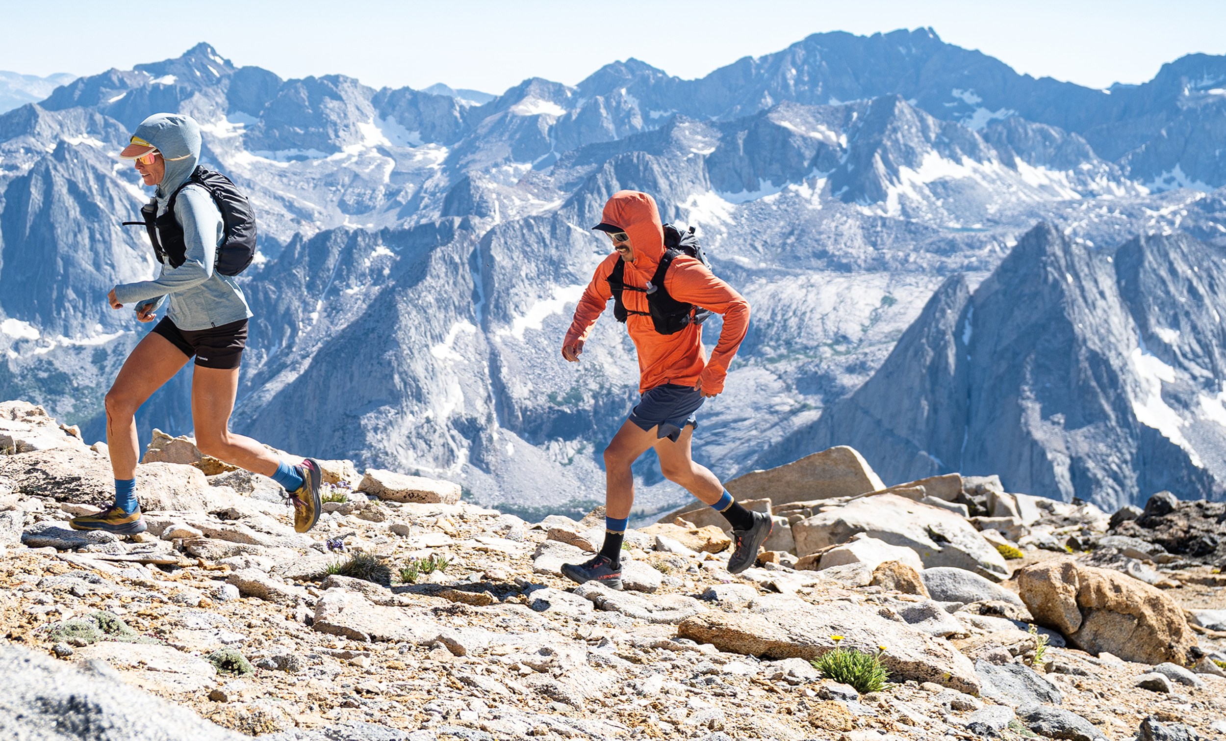 Two hikers dressed in colorful outdoor Patagonia gear hiking on rocky terrain with snow-capped mountain peaksnear Yellowstone National Park and Bozeman, Montana.