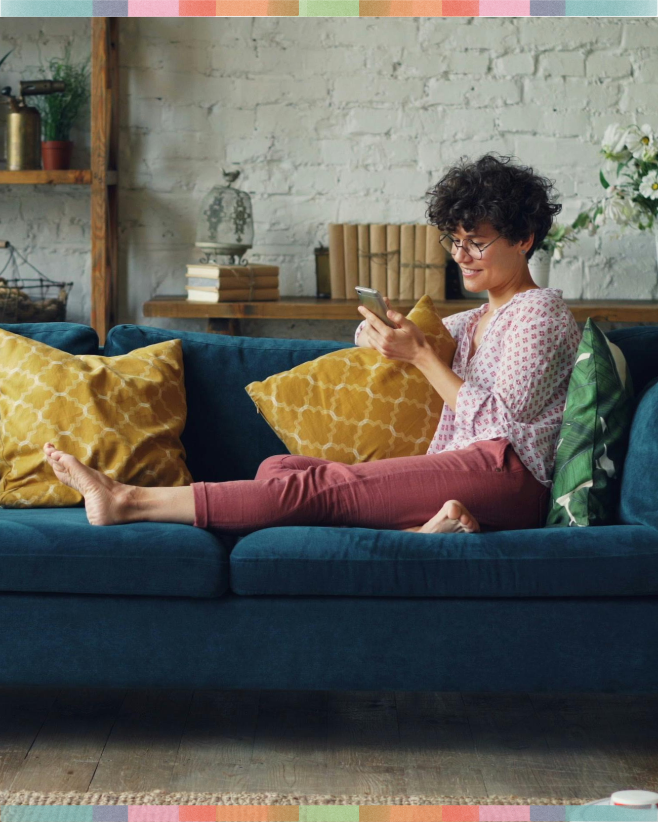 Woman smiling at her phone while relaxing on a blue couch at home