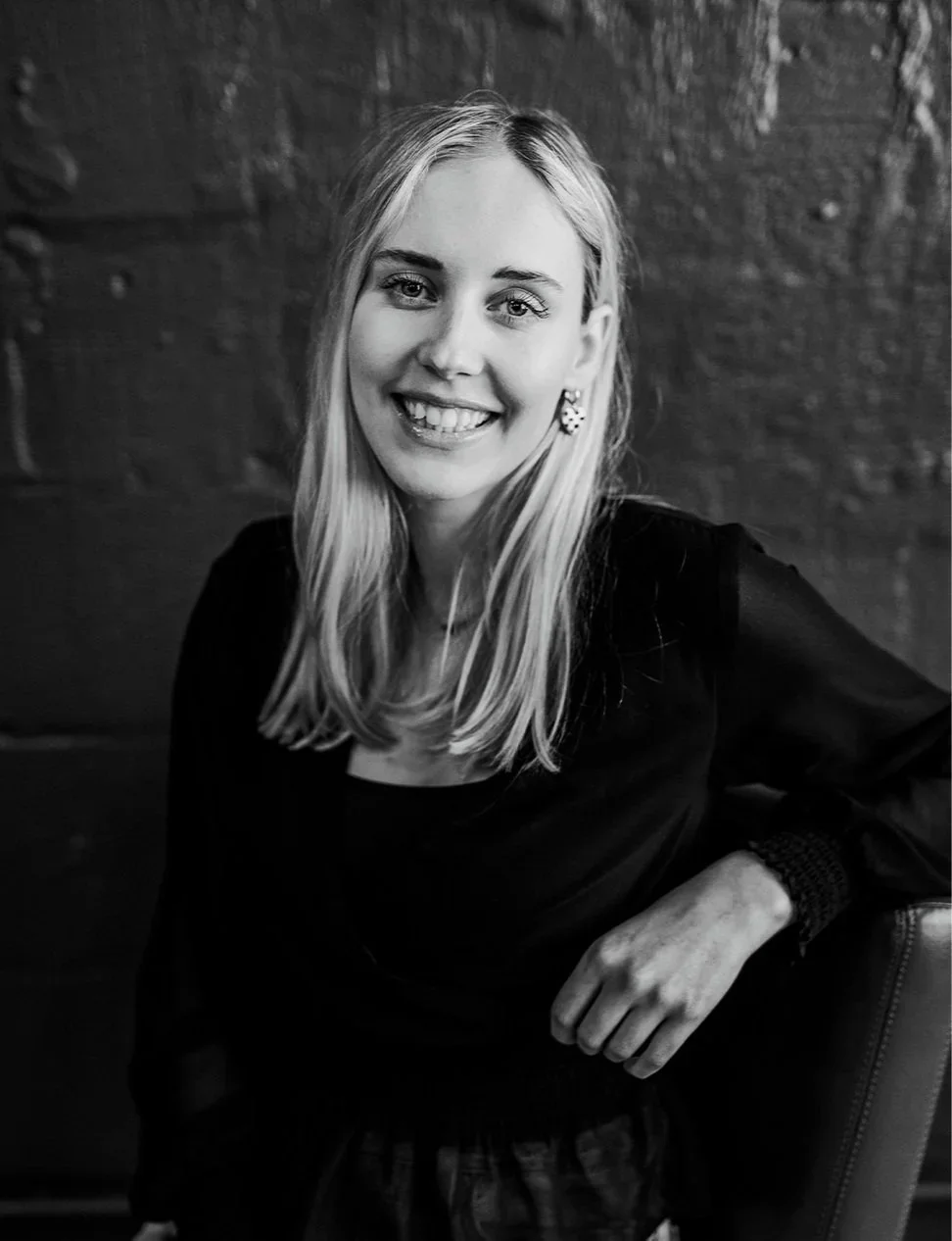 Black-and-white portrait of a smiling blonde woman wearing a black top and earrings.