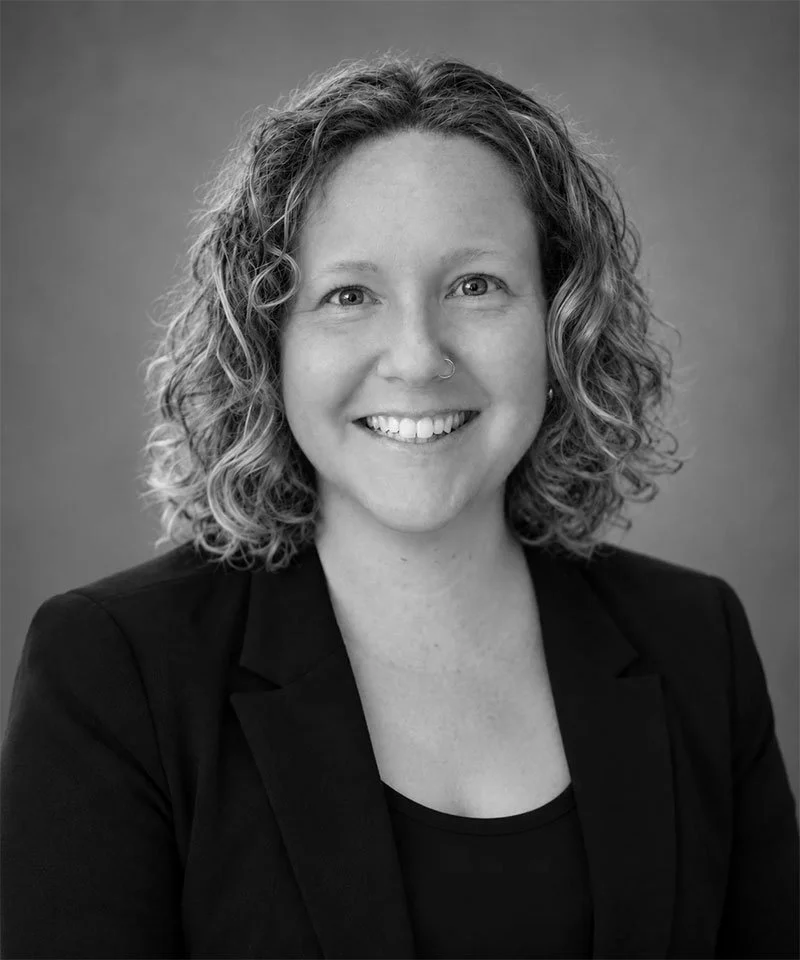 Black-and-white professional headshot of a smiling woman with curly hair wearing a blazer.