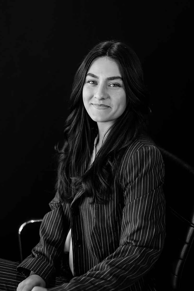 Black-and-white portrait of a smiling woman with long dark hair wearing a pinstriped blazer.