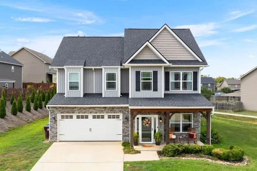 Front view of a two-story suburban house with a front porch, attached garage, and well-maintained yard.