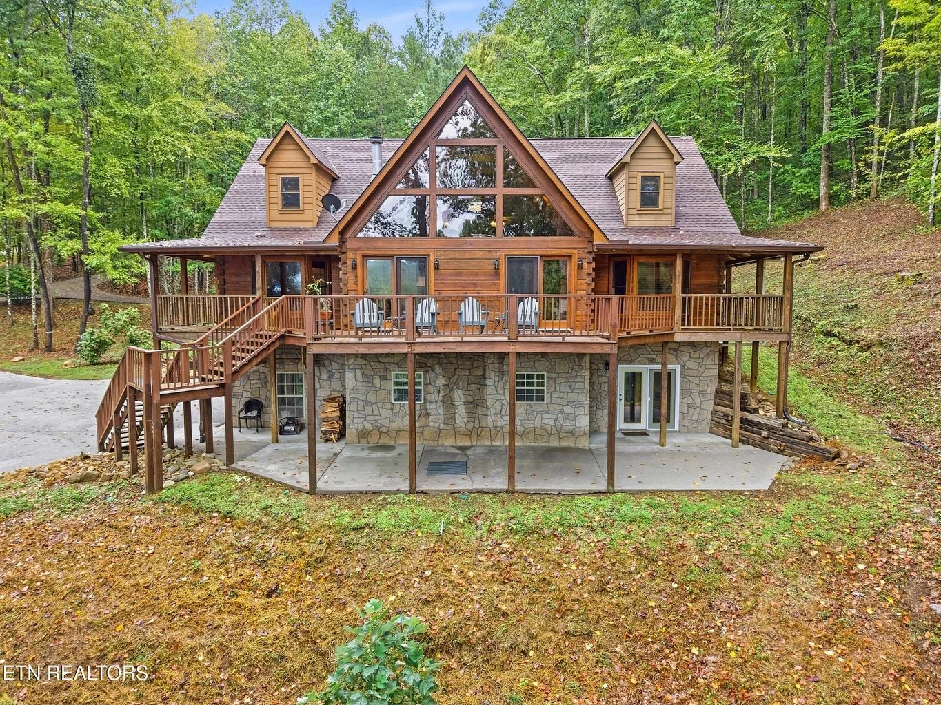 Wooden house with a large stained glass window at the front, balconies, and a stone foundation, surrounded by trees.