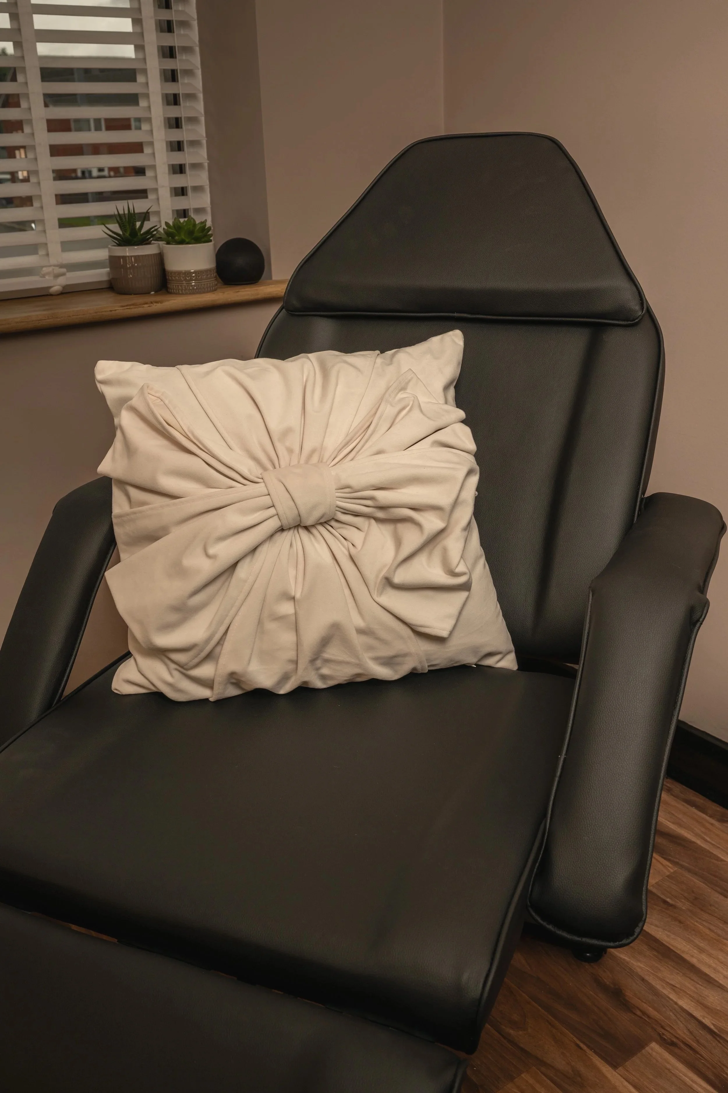 Black treatment chair with an ivory cushion beside a window in the clinic.