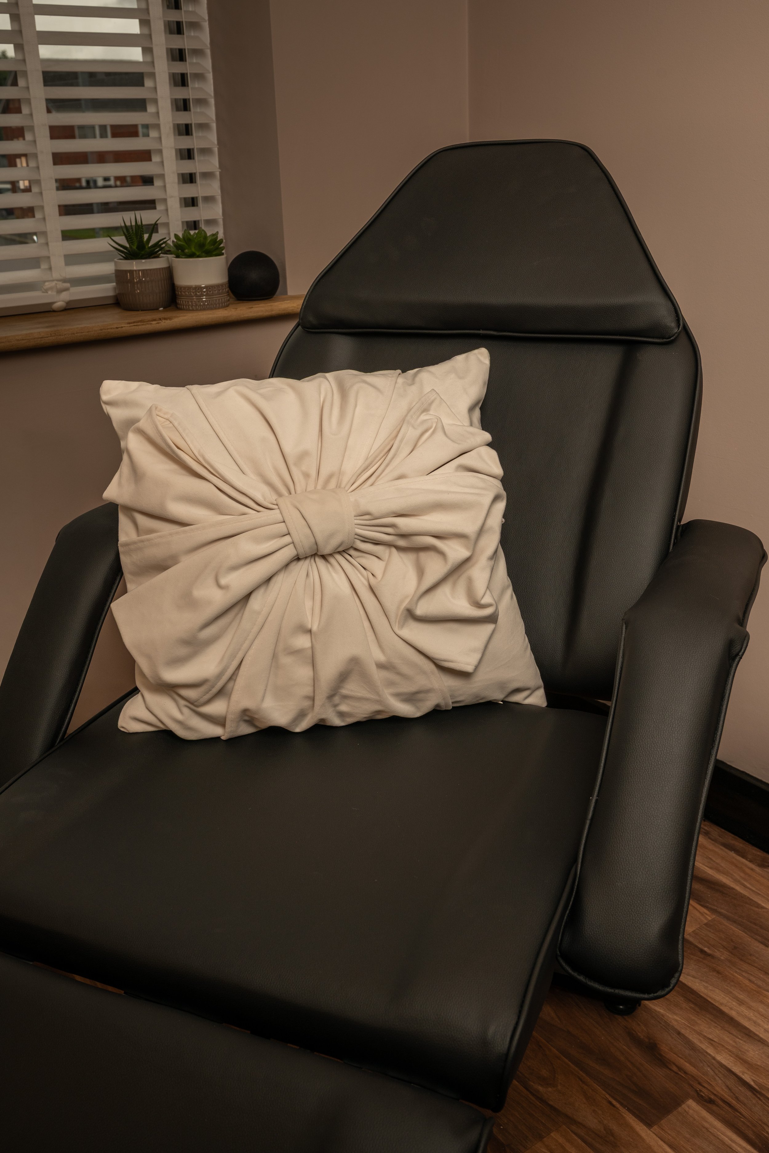 Black treatment chair with an ivory cushion beside a window in the clinic.