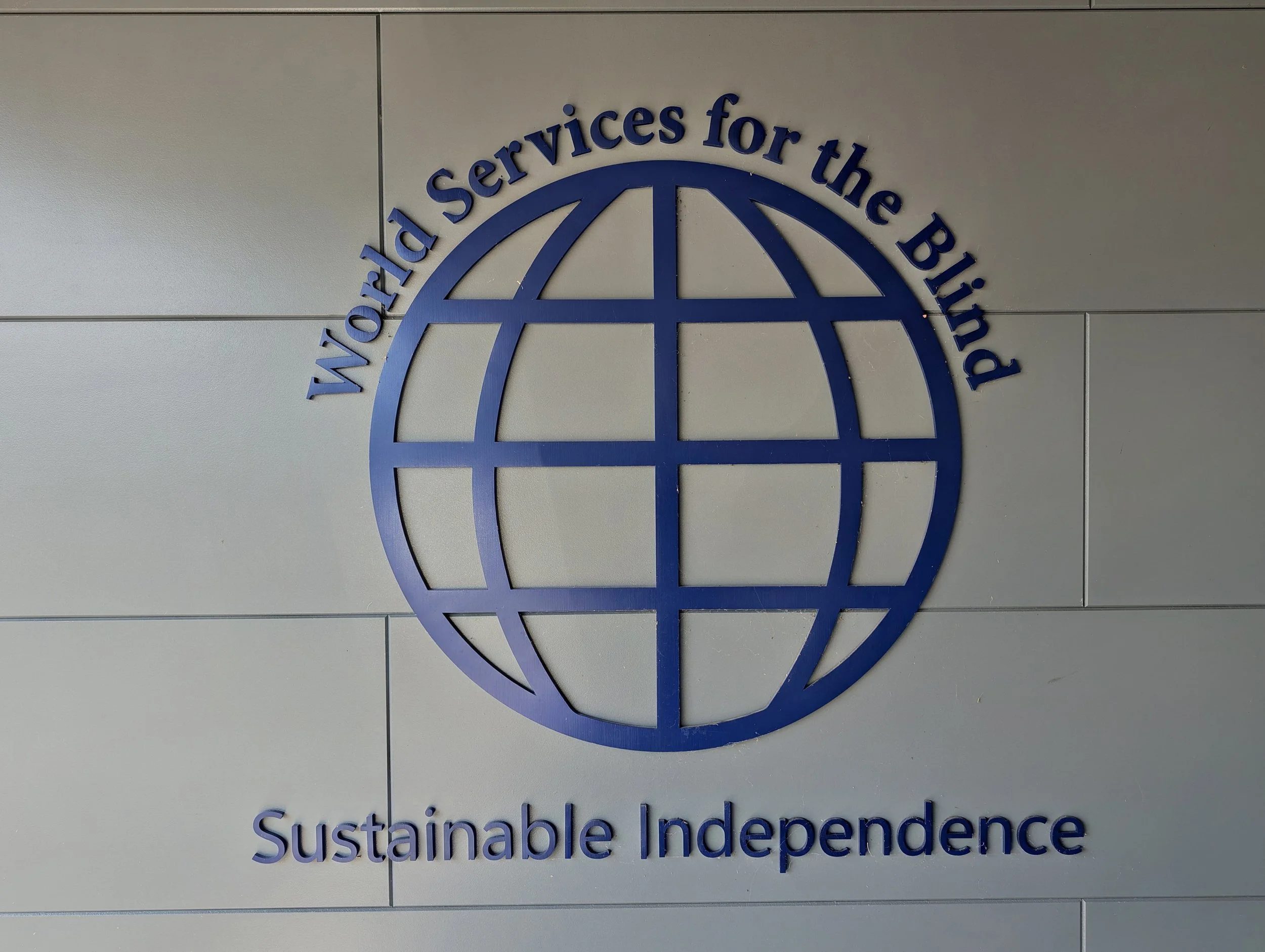 Sign on wall of WSB with a globe surrounded by the words "World Service for the Blind. Sustainable Independence."