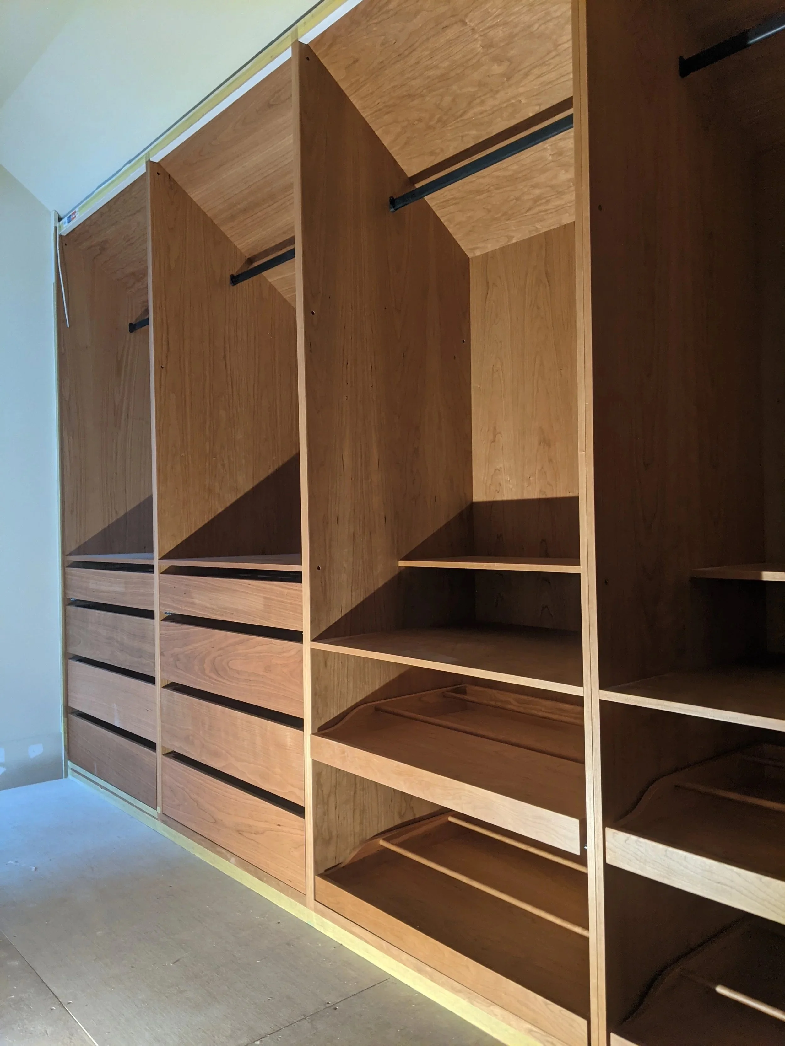 Empty wooden shelving units with multiple compartments and drawers, installed against a wall with some yellow painter's tape and a beige wall, on a carpeted floor.