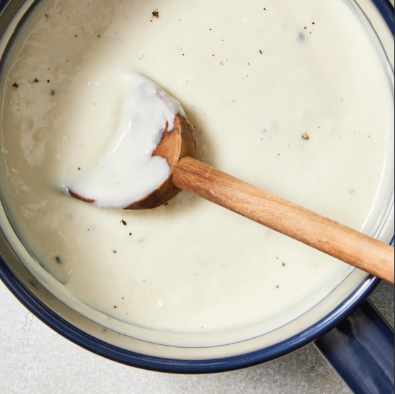 A pot of creamy white gravy being stirred with a wooden spoon.