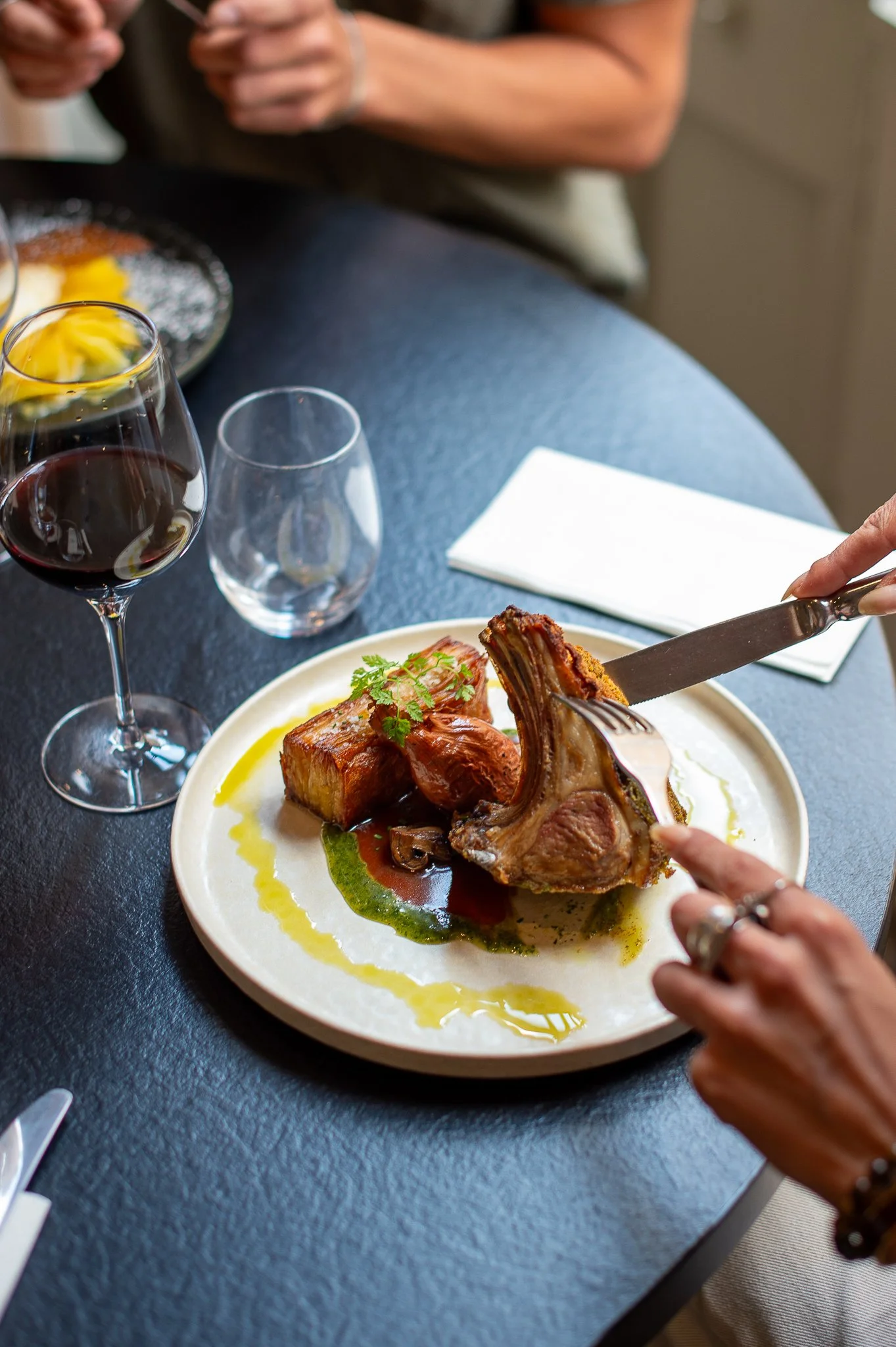 Une assiette avec une portion de viande et un gratin, accompagnée d'un verre de vin rouge sur une table.