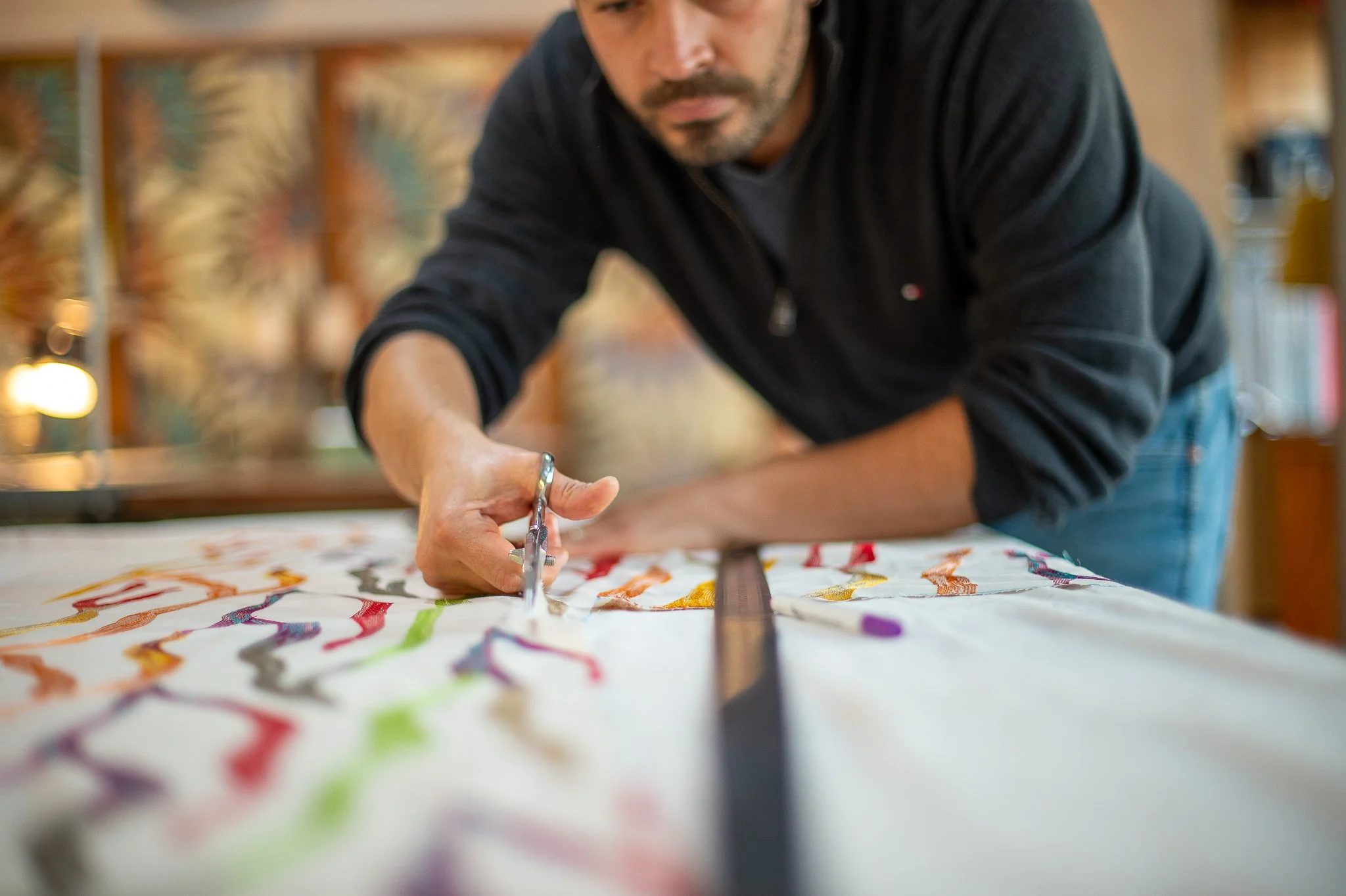 Un homme qui coupe un tissu avec des ciseaux, examinant les motifs colorés