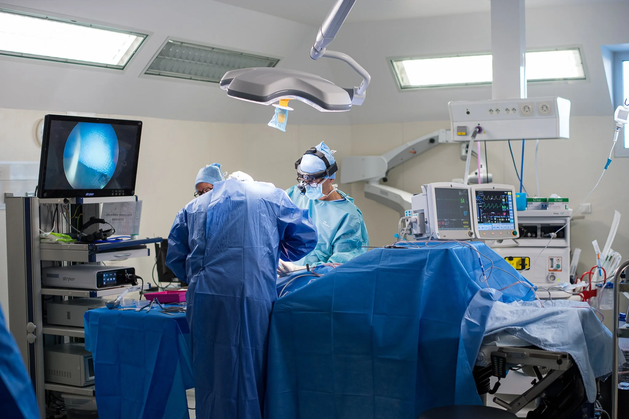Opération chirurgicale dans une salle d'opération avec des médecins en train de travailler, plusieurs moniteurs médicaux, une lumière chirurgicale, et du matériel médical.