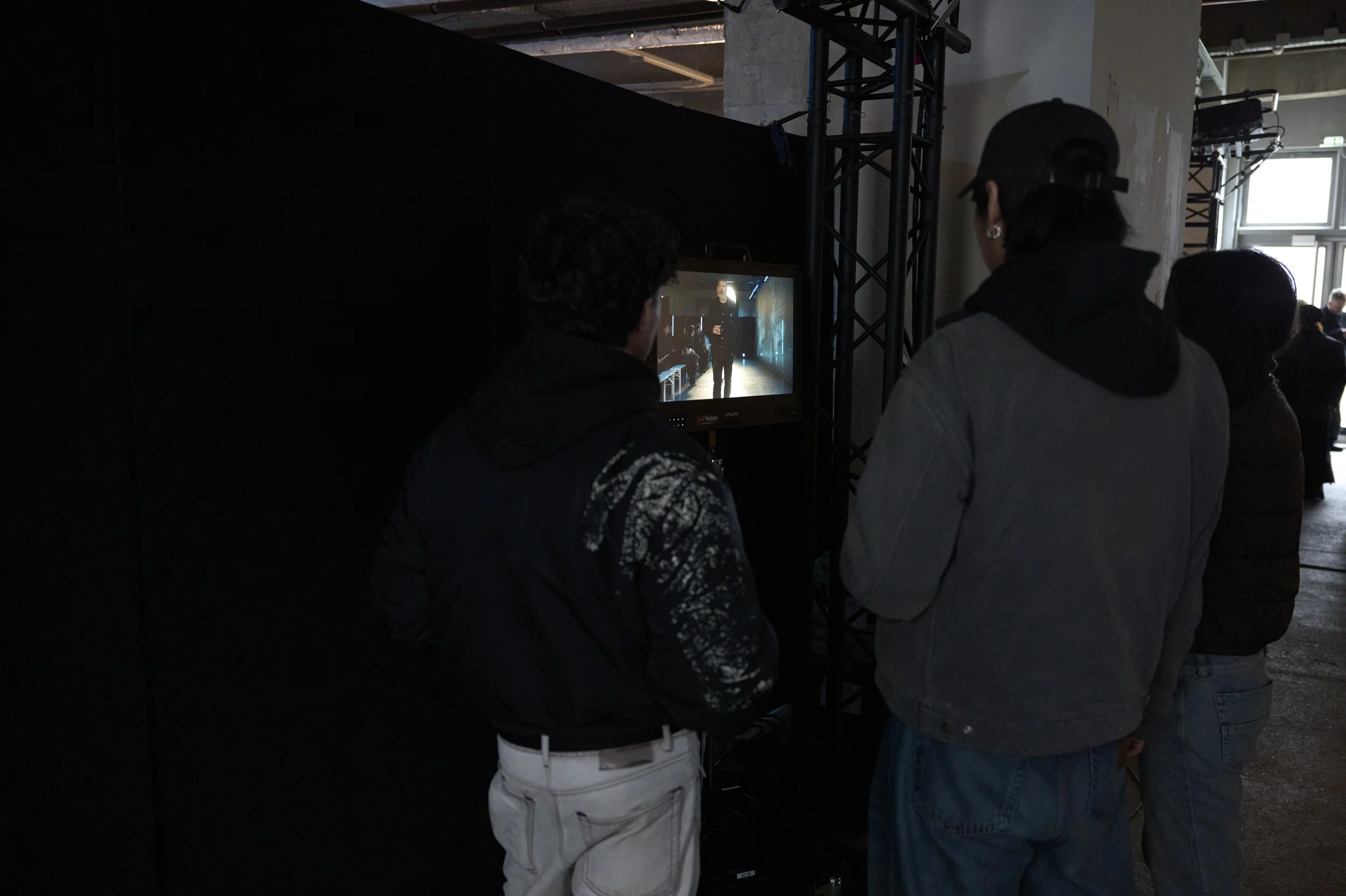 Des visiteurs regardent un écran affichant une personne sur une scène, dans un espace événementiel équipé de structures d’éclairage.