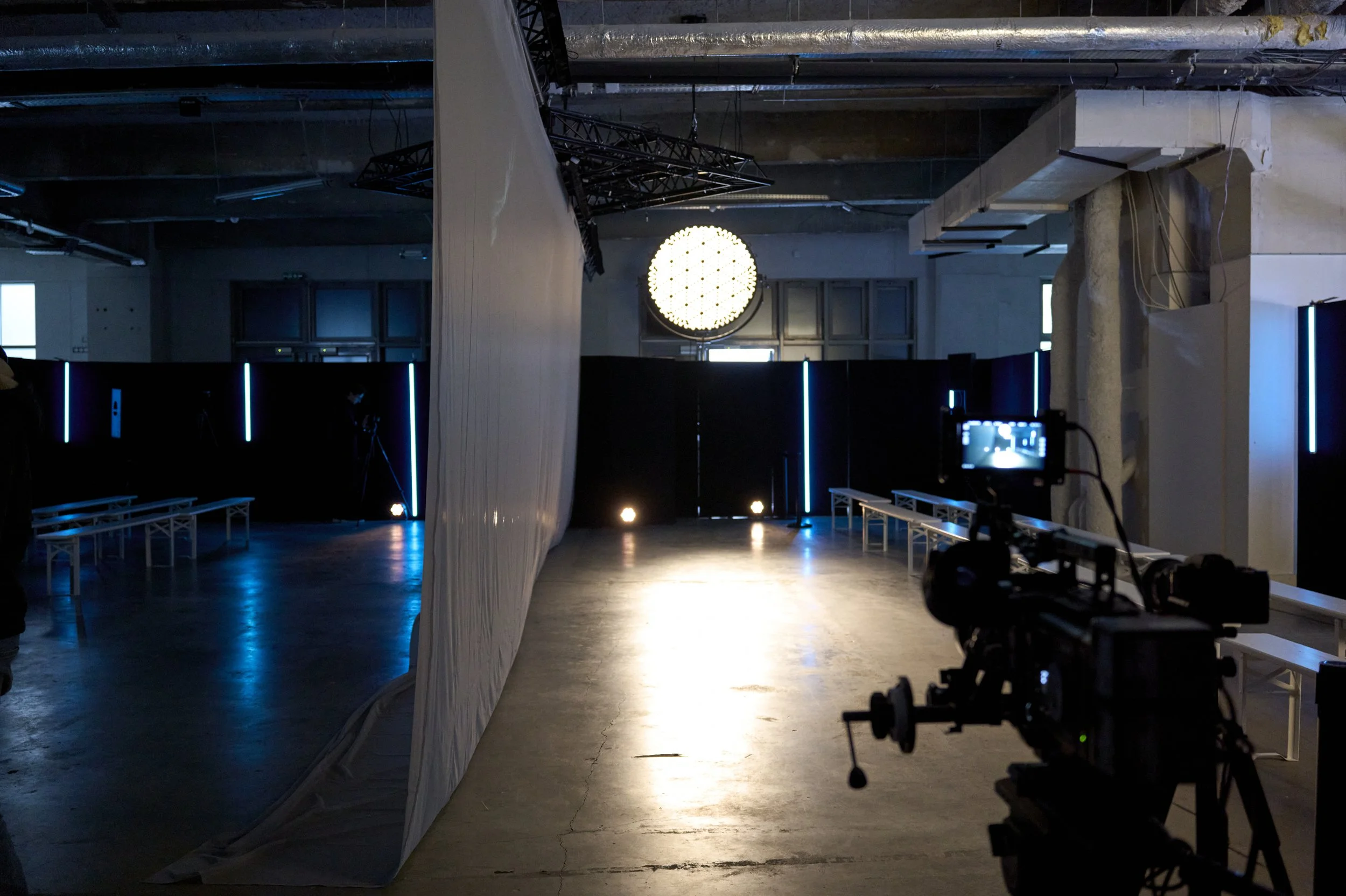Plateau de tournage sombre avec éclairage bleu, projecteurs, bancs et caméra professionnelle au premier plan.