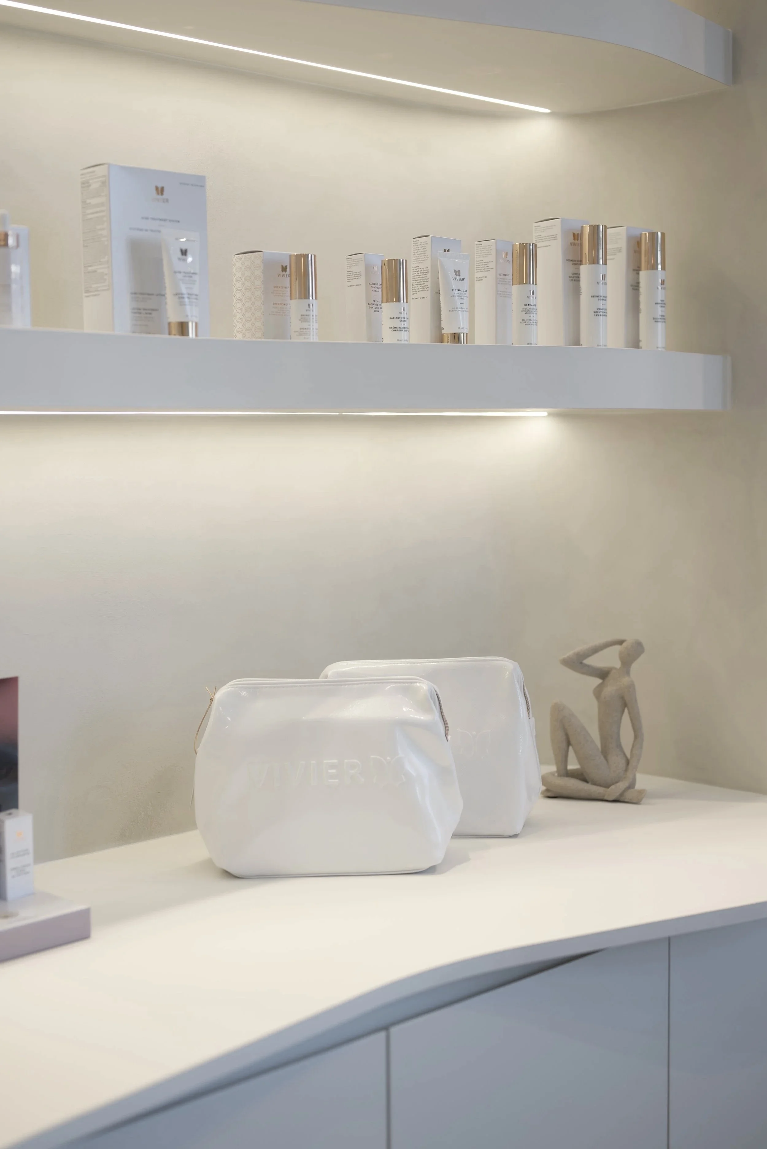 Une étagère blanche avec des tubes et boîtes de produits de soin ou cosmétiques, et une sculpture abstraite en arrière-plan.