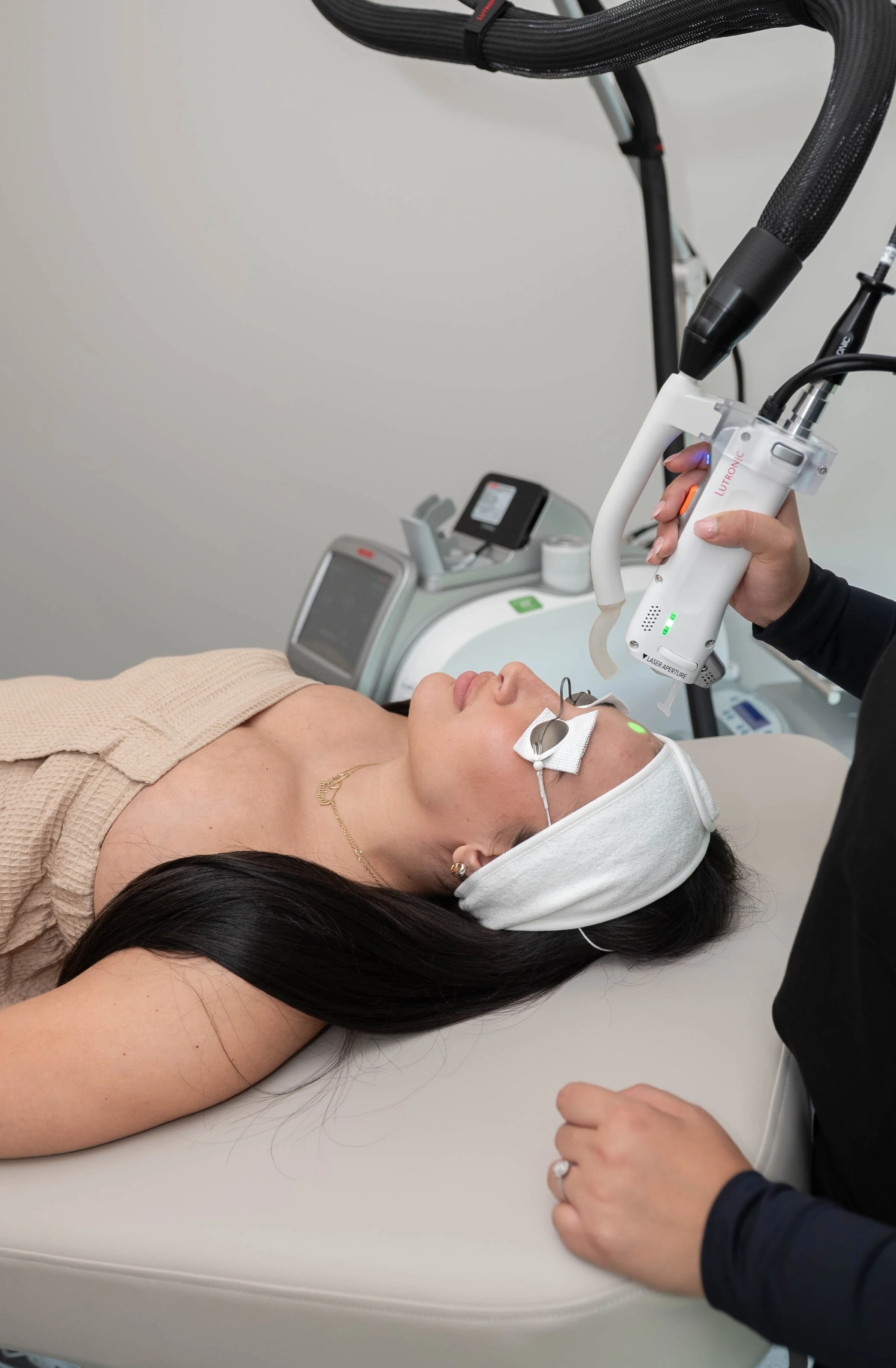 Une femme reçoit un traitement médical avec un appareil de laser sur le visage, allongée sur une table d'examen, sous la supervision d'un professionnel de santé.