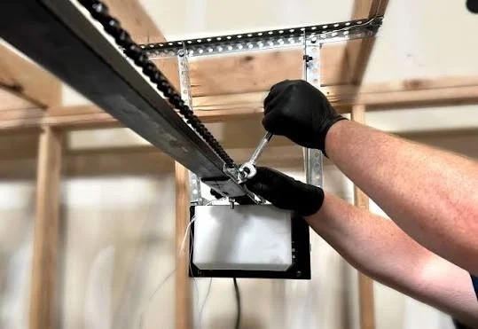 A person wearing black gloves using a wrench to tighten or loosen a bolt on a metal frame in a garage or workshop setting.