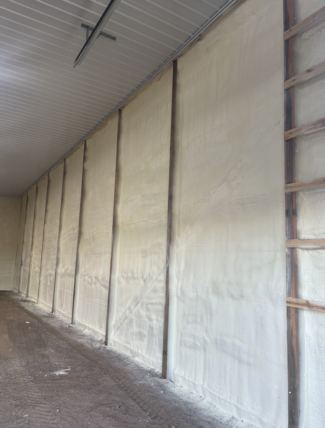 Insulated wall in a construction site with drywall foam insulation installed between wooden framing studs and a metal ceiling.
