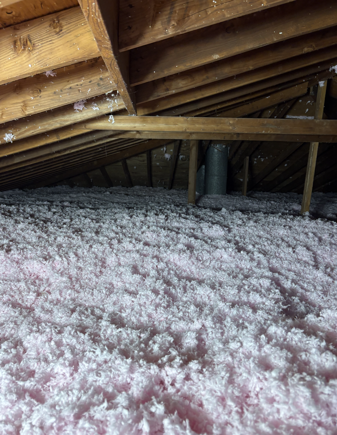 View of an attic with wooden beams and a snow-covered floor.