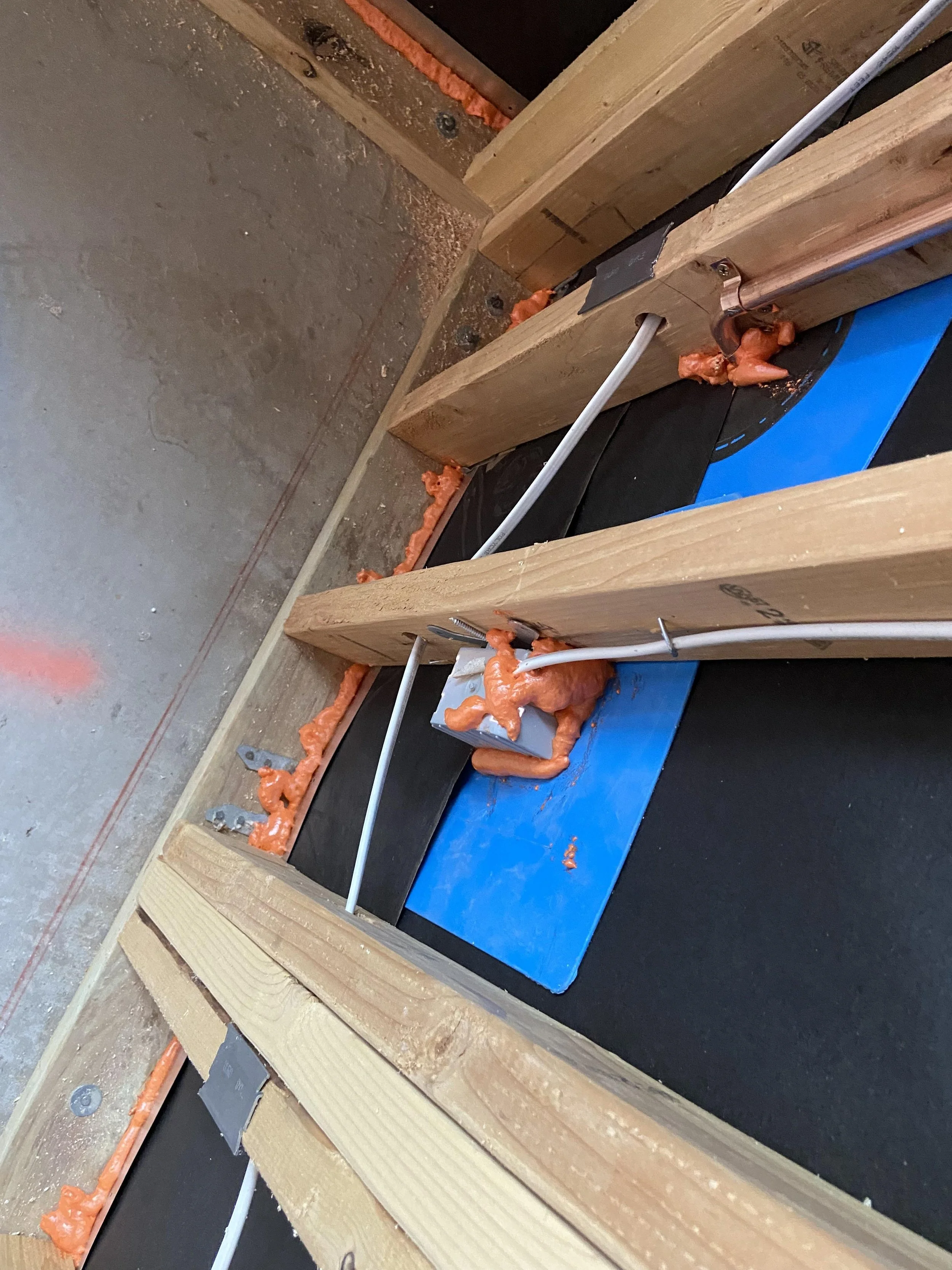 Close-up view of framing work inside a building, showing wooden studs, electrical conduit, and orange foam insulation.