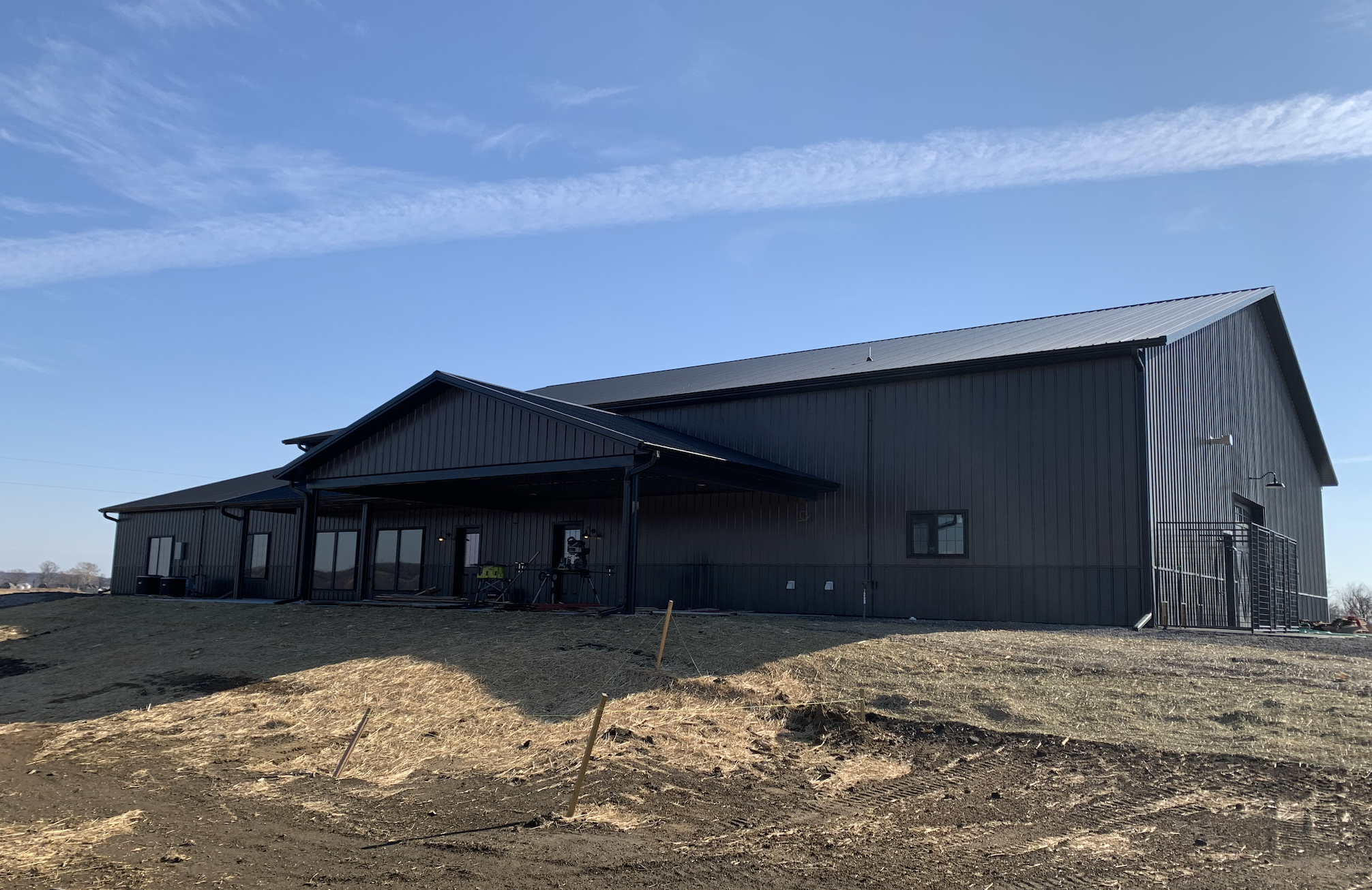 A large, modern metal building with a sloped roof, several windows, and a porch with bicycles outside under a clear blue sky.