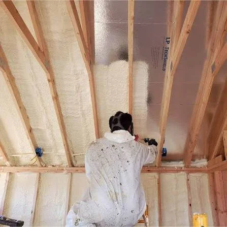 A worker installing or repairing insulation in a building's ceiling framework.