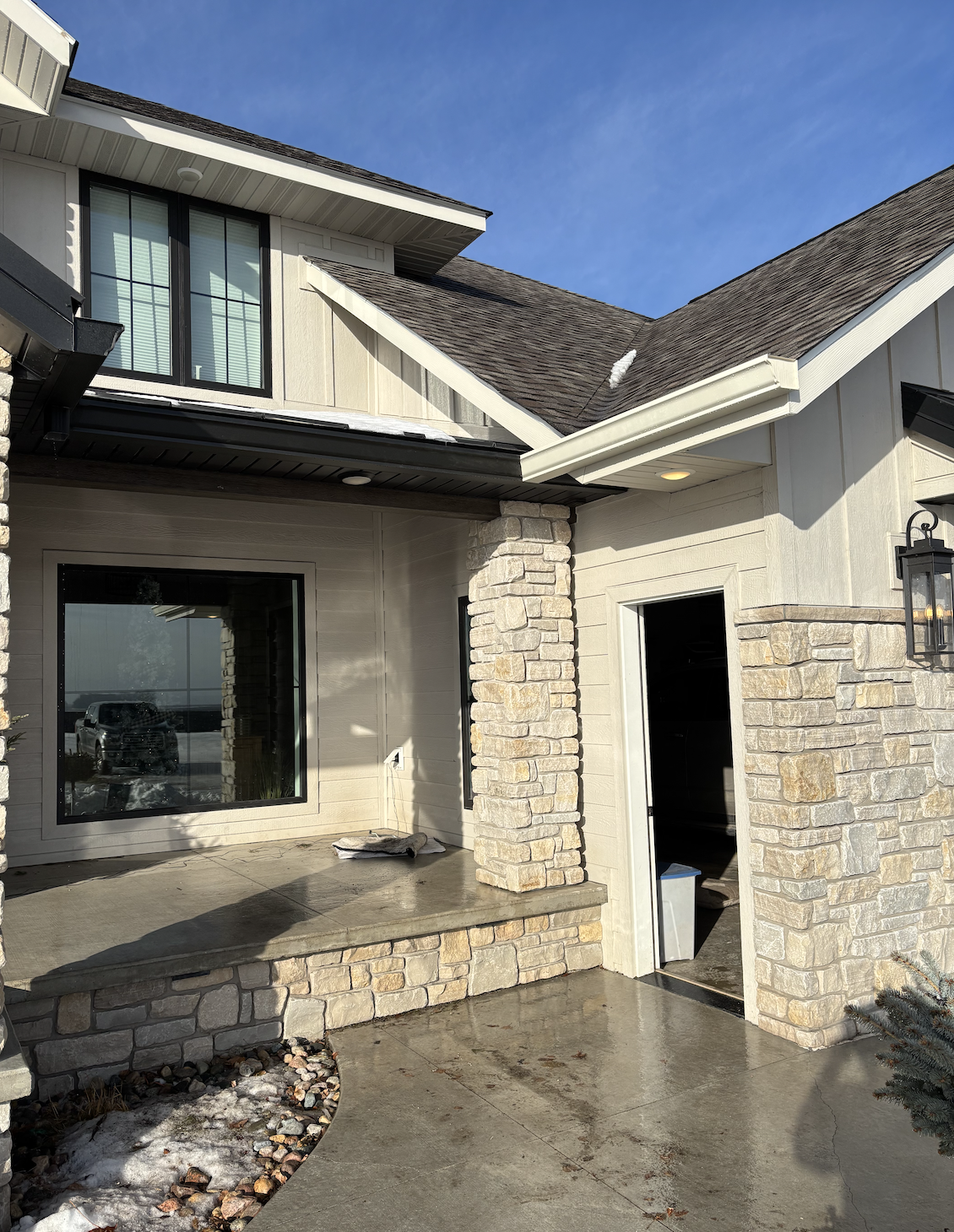 Front of a house with large windows, stone accents, and a small porch under a blue sky.