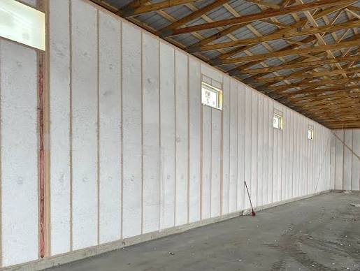 Interior view of a building under construction with a framed wall, small rectangular windows, and unfinished concrete floor.