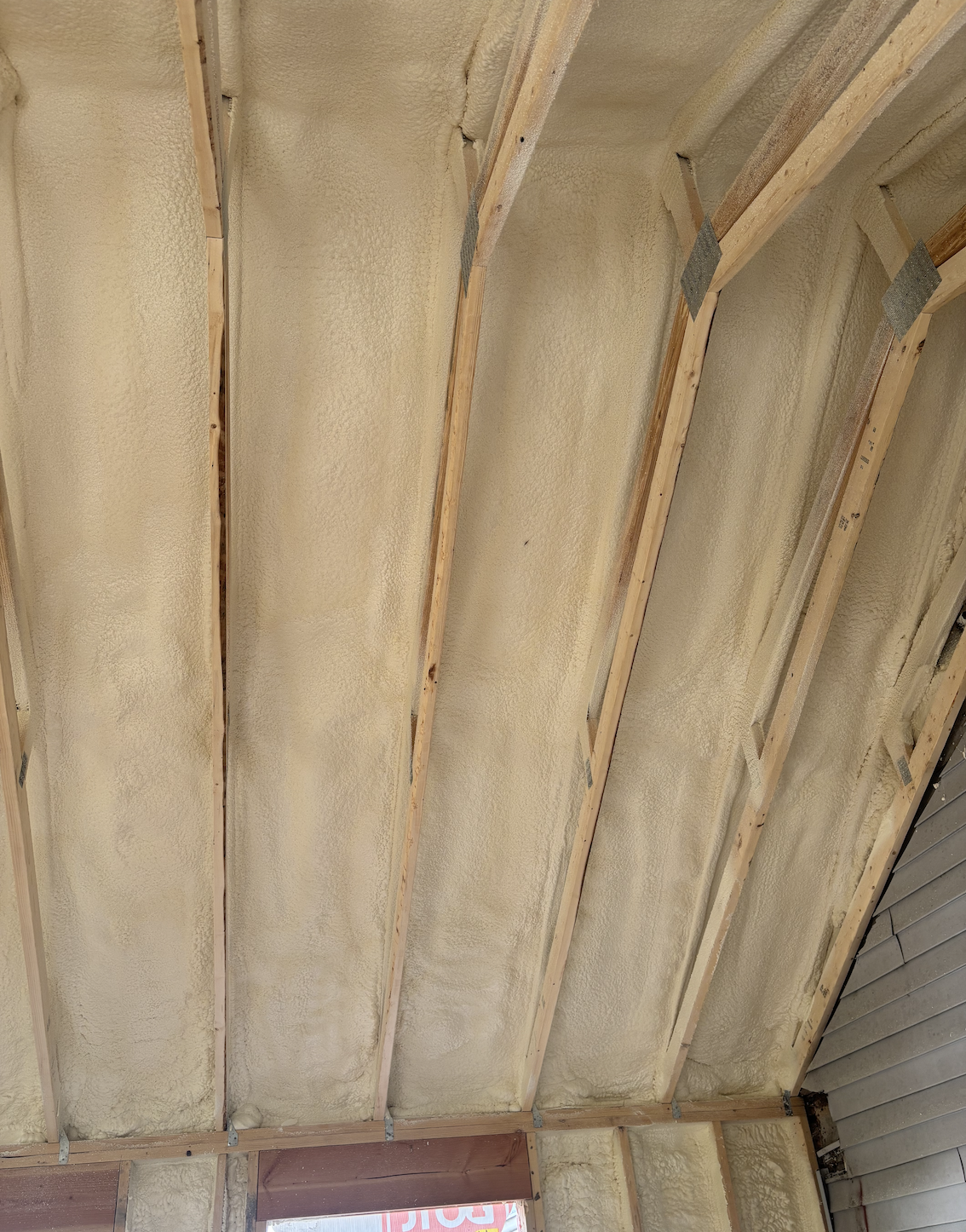 Insulated ceiling with wooden beams and foam spray insulation installed.