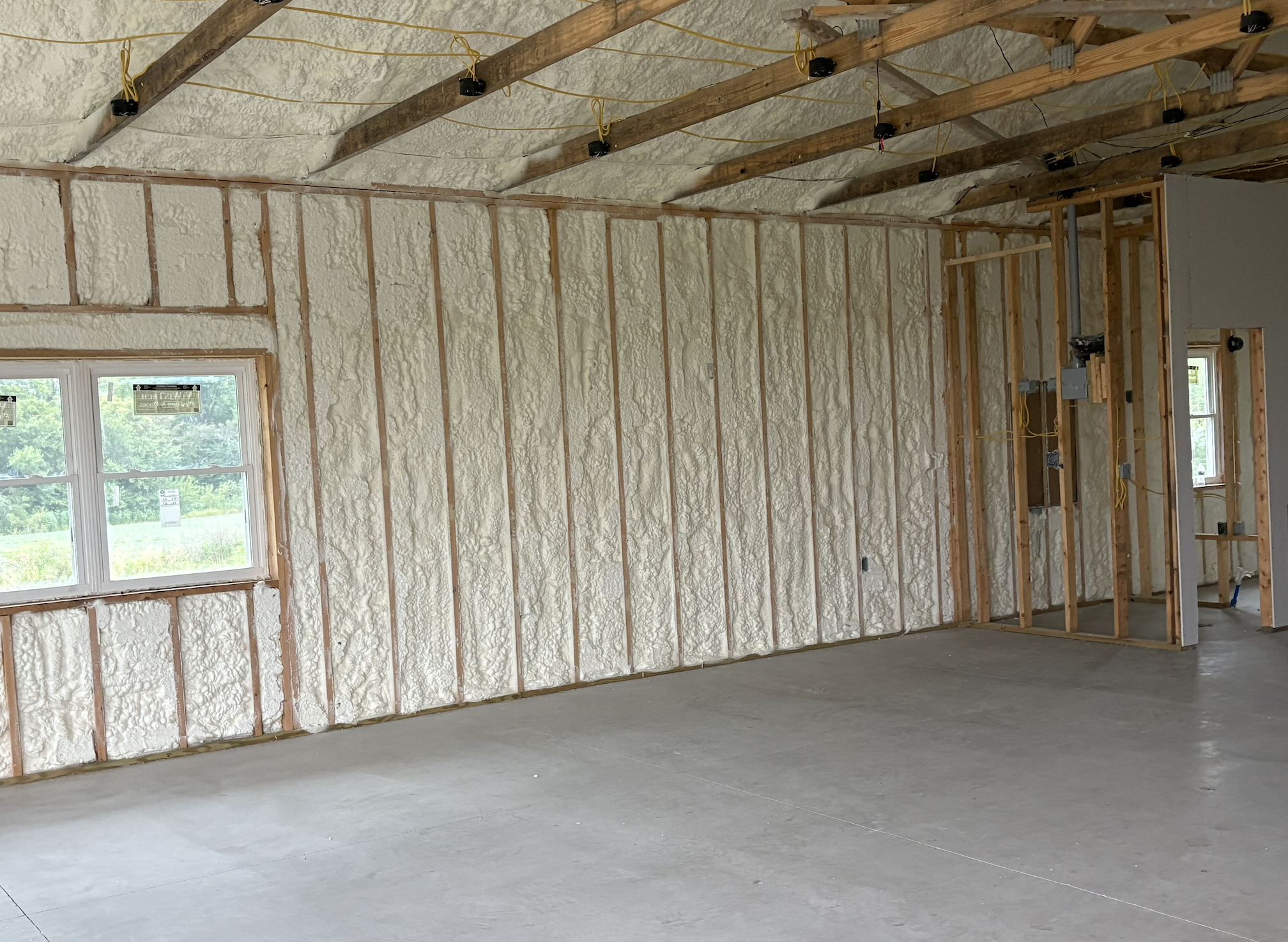 Interior of a house under construction with spray foam insulation on the walls and ceiling, wooden studs, and exposed electrical wiring.